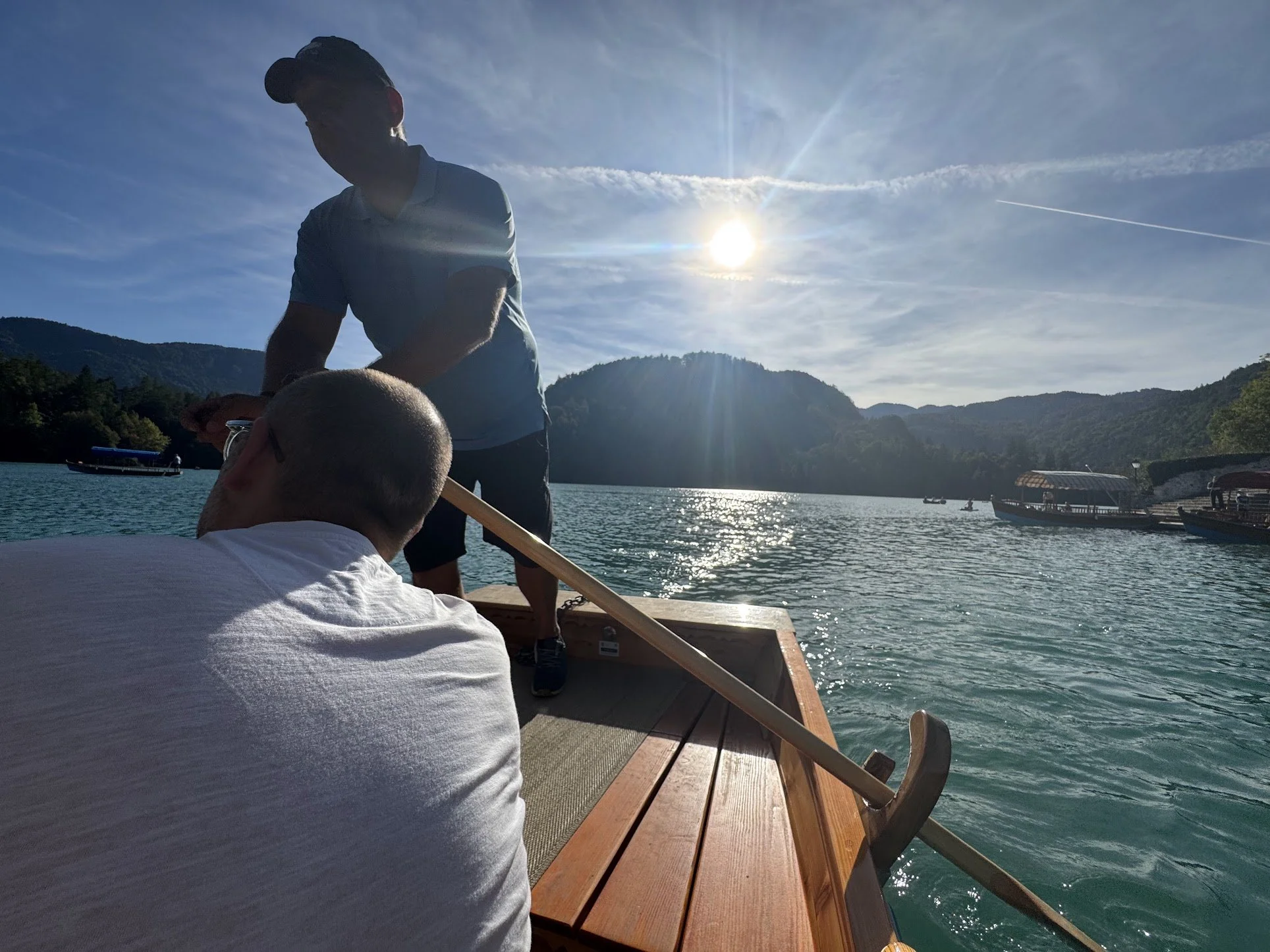 People on a boat floating on a lake with mountains in the background, the sun shining in the sky.