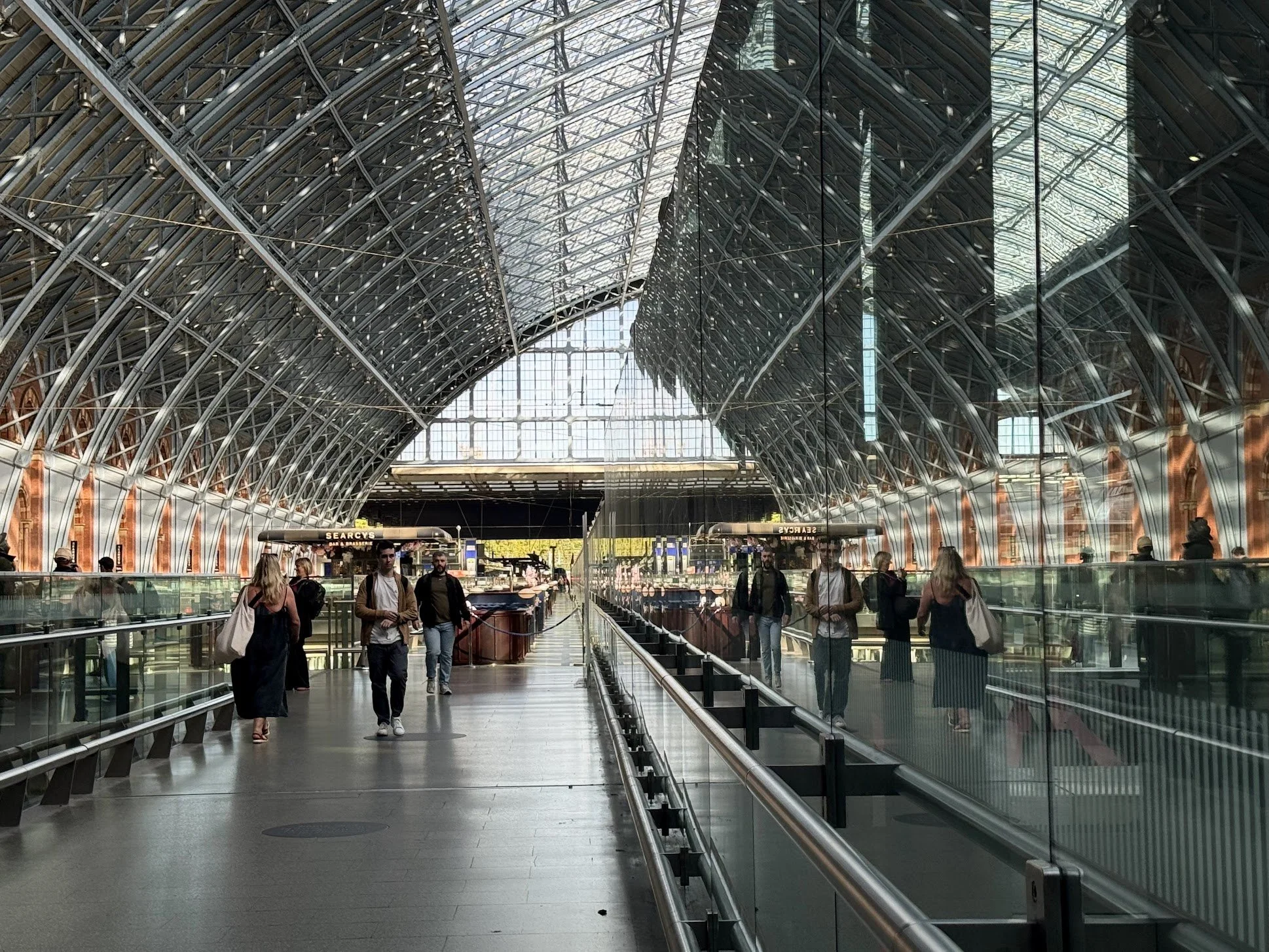 People walking inside a modern train station with high arched glass and steel ceiling and large windows letting in natural light.
