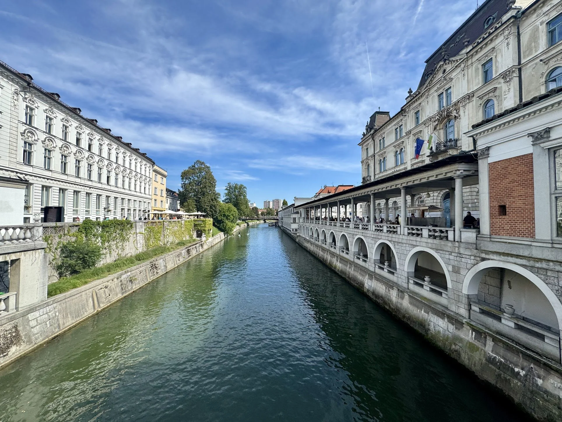 View of a river flanked by historic European-style buildings with ornate facades, under a partly cloudy blue sky.