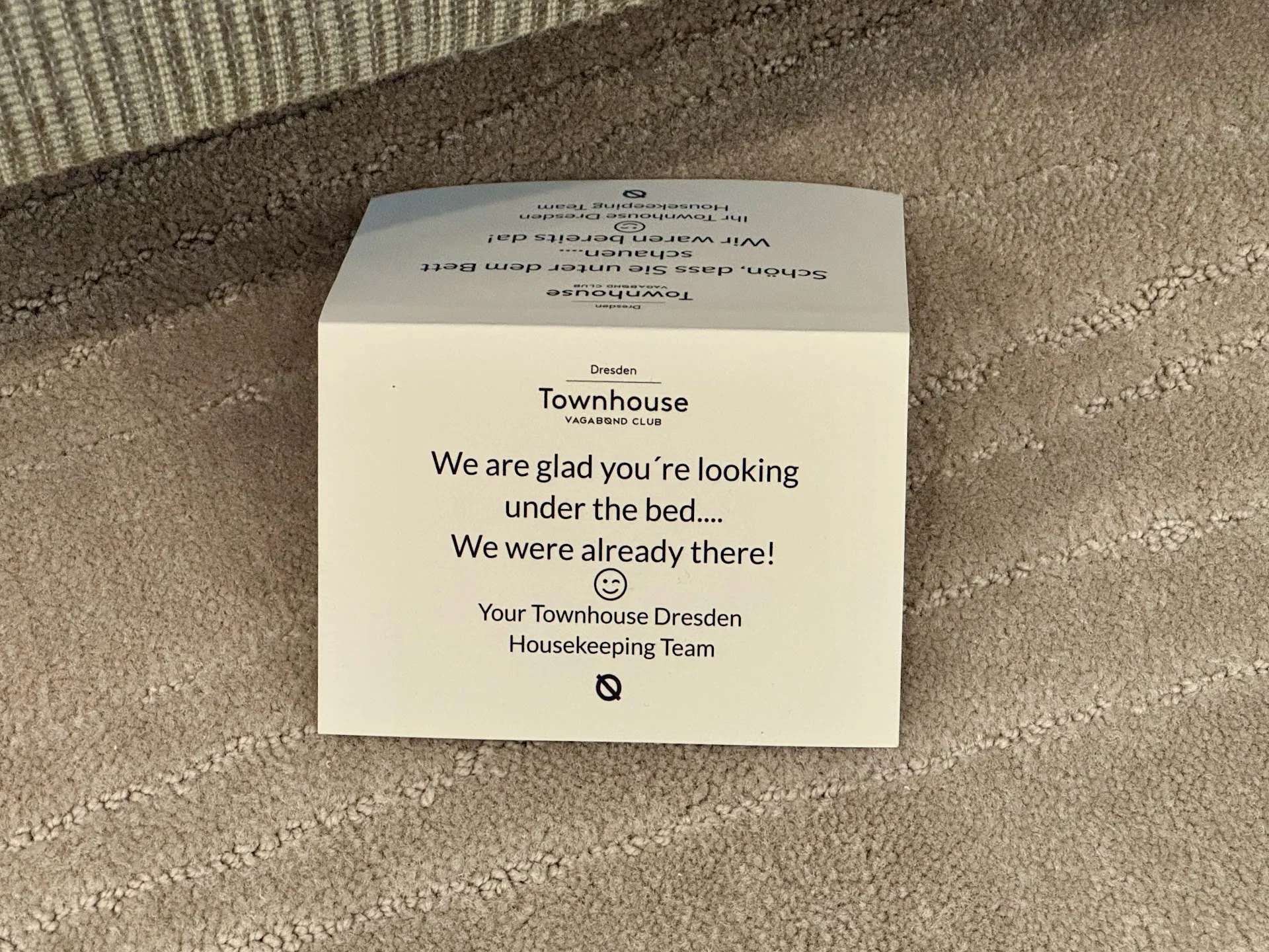 A note on a beige textured carpet indicating that you are looking under the bed, from the Townhouse Dresden Housekeeping Team.