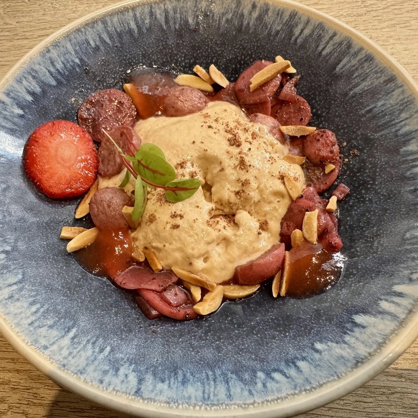 A dessert plate with vanilla ice cream, sliced strawberries, sliced almonds, and cherry compote garnished with a small green leaf.