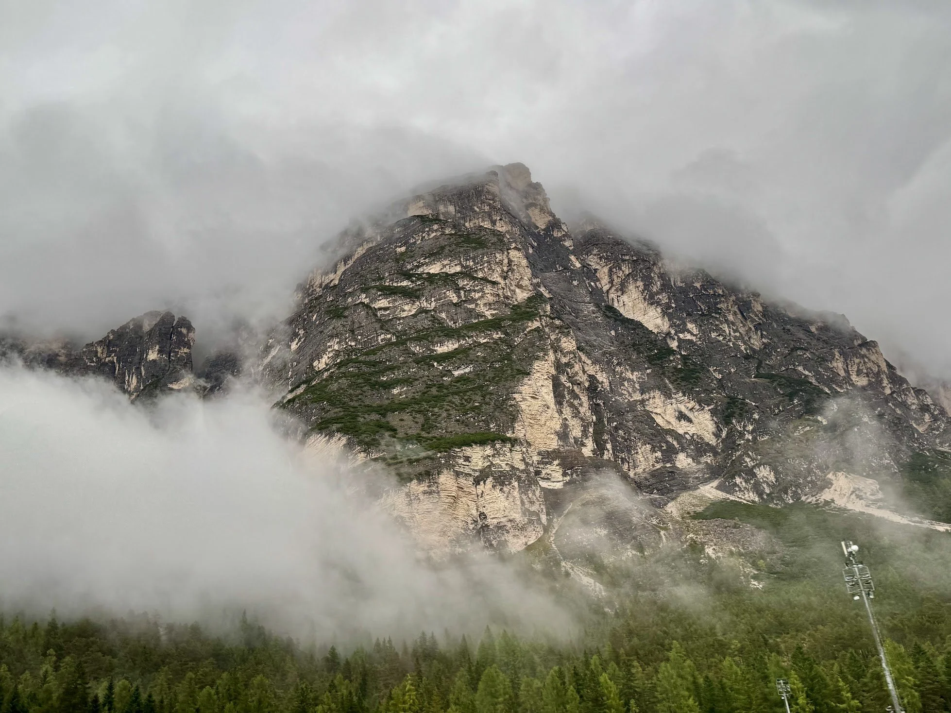 A mountain partially covered by mist or clouds, with greenery at the base.