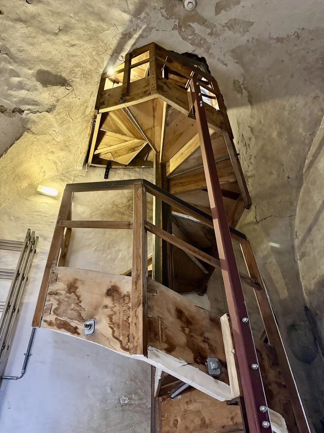 Interior view of a spiral staircase under construction with wooden steps and railings, no handrails installed yet, surrounded by unfinished concrete walls.