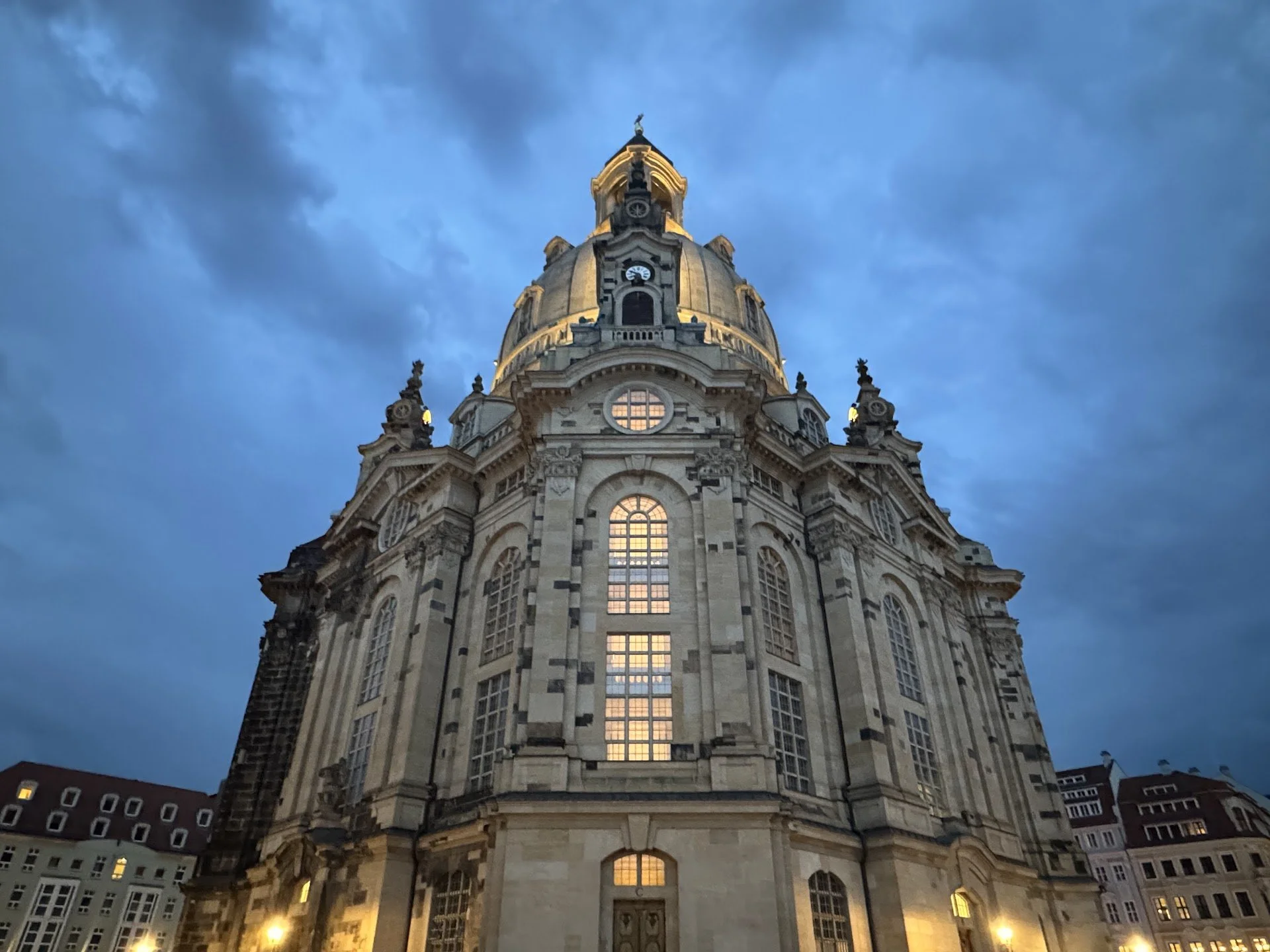A historic domed building lit up at dusk with a cloudy sky background.