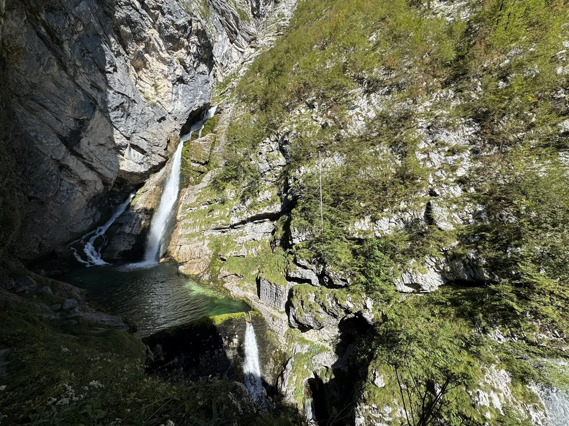 A waterfall flowing down a rocky cliff surrounded by lush green forest with clear water at the bottom.