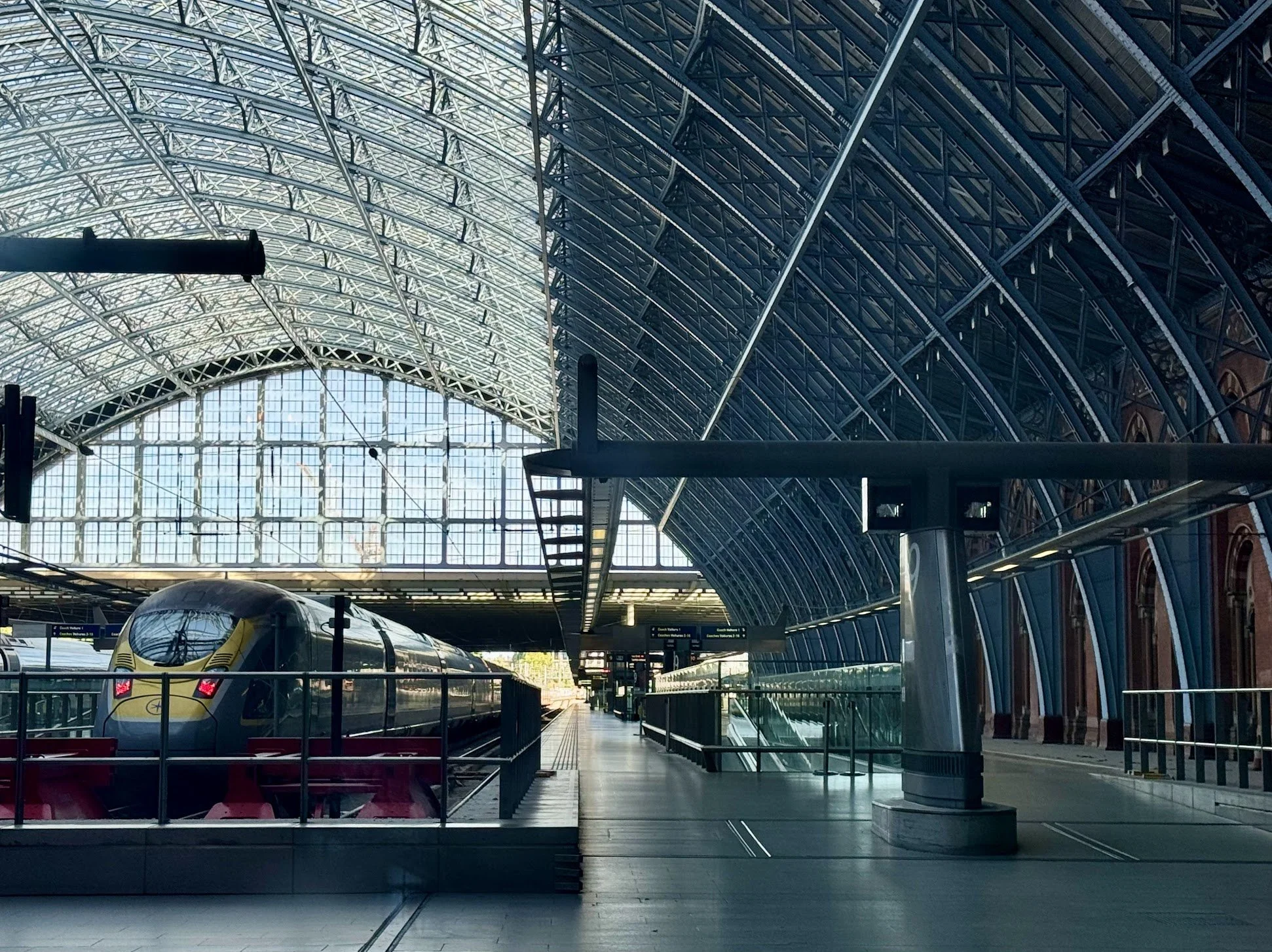 Interior of an airport terminal with a high arched glass ceiling, a modern train on the platform, and various signage visible in the background.