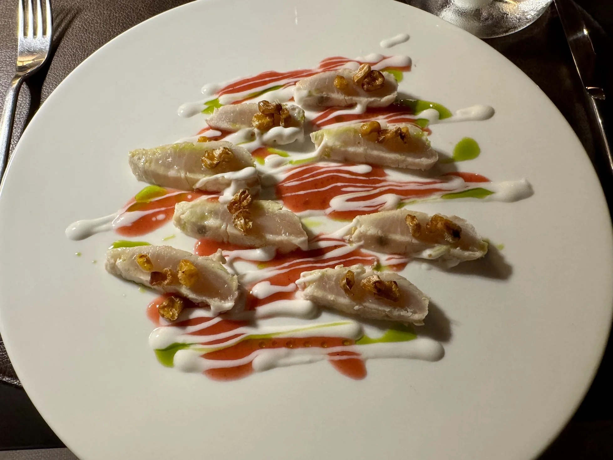 Sliced fish or chicken roulade topped with chopped nuts and drizzled with white, red, and green sauces, served on a white plate.