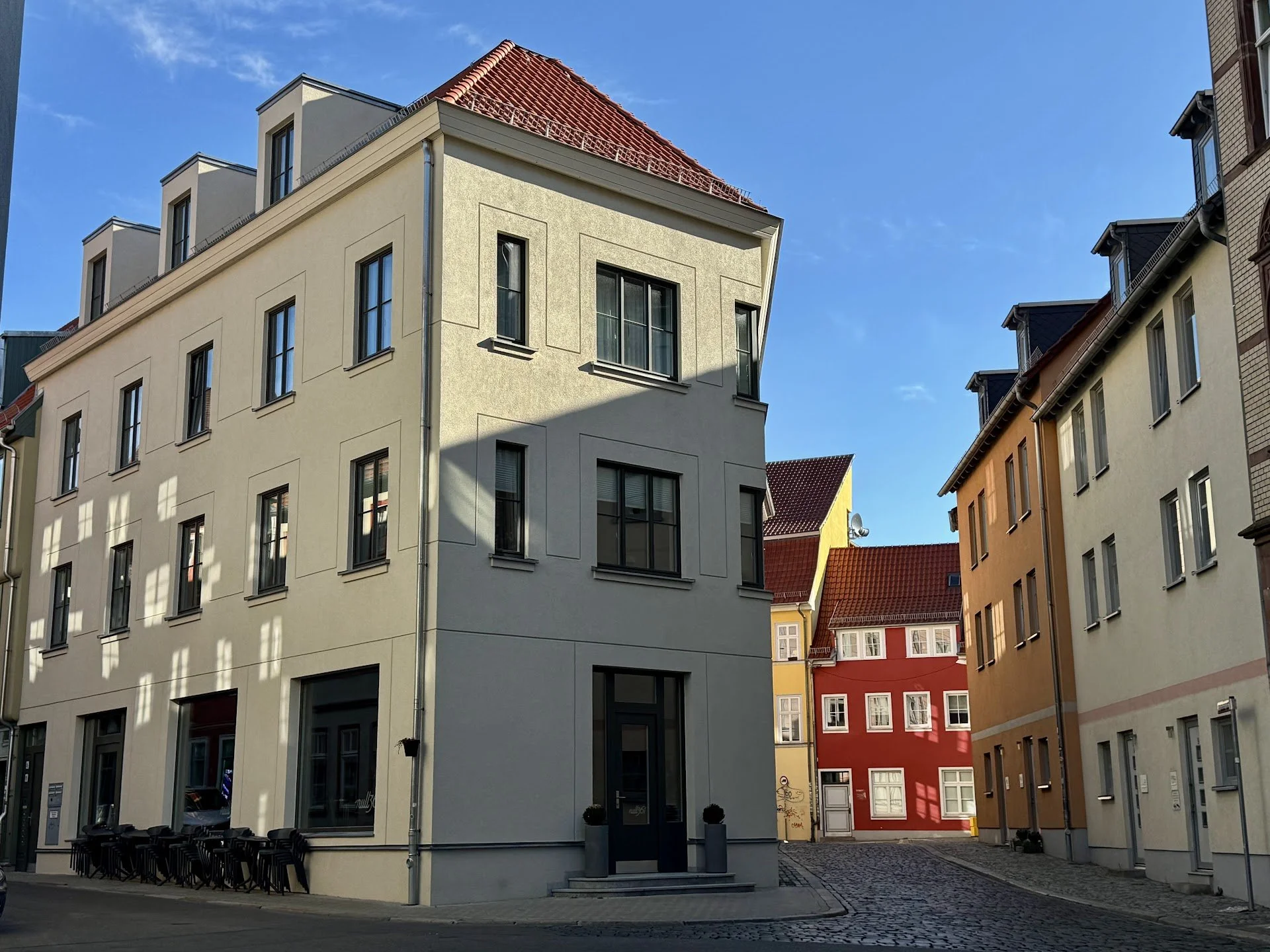 City street view showing multi-story buildings with colorful facades, such as yellow, red, and beige, under a clear blue sky.