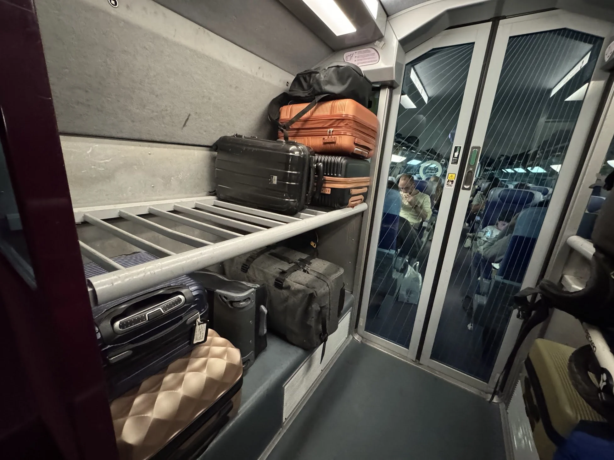 Luggage and bags are stored on a luggage rack inside an airport shuttle bus. The bus has a glass door and a man is visible inside.
