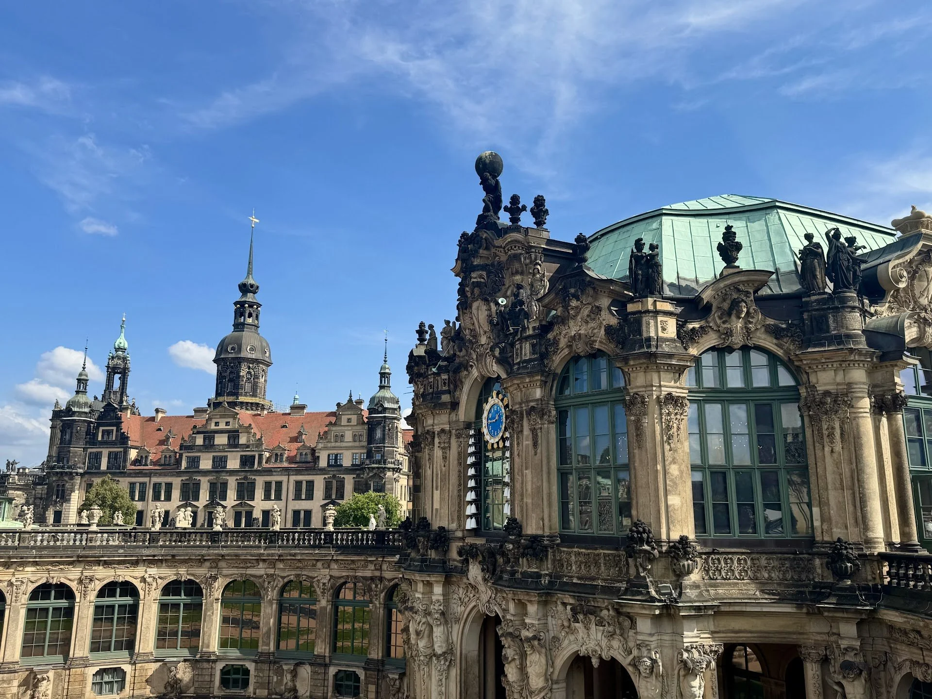 View of an ornate historic building with sculptures and a glass dome, against a blue sky with clouds.