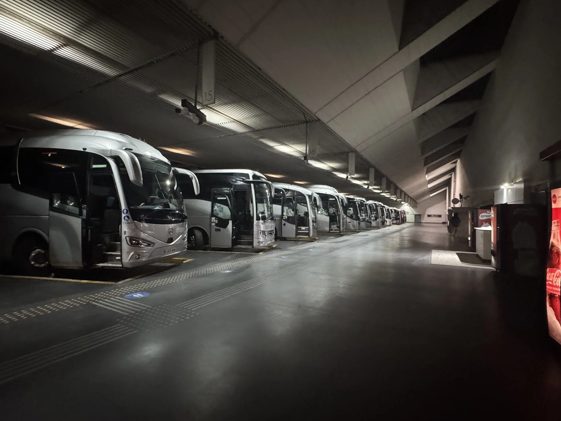 Underground bus station with multiple parked buses and a person walking nearby, illuminated by overhead lighting.