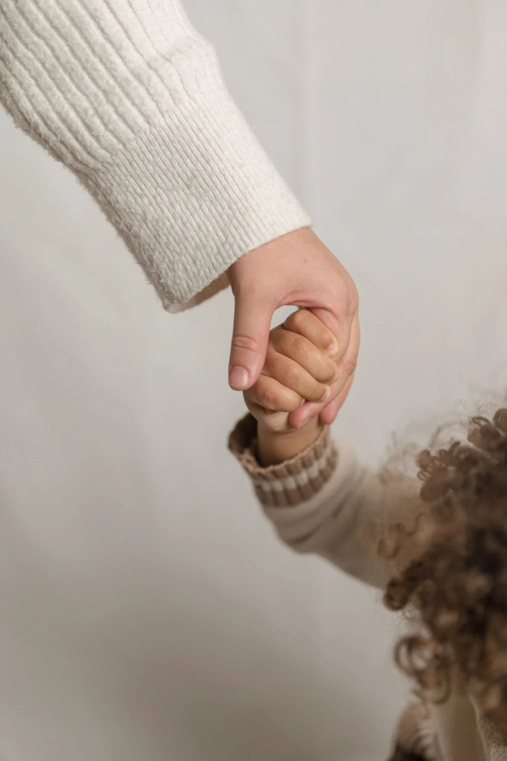 An adult's hand holding a child's hand against a plain background.