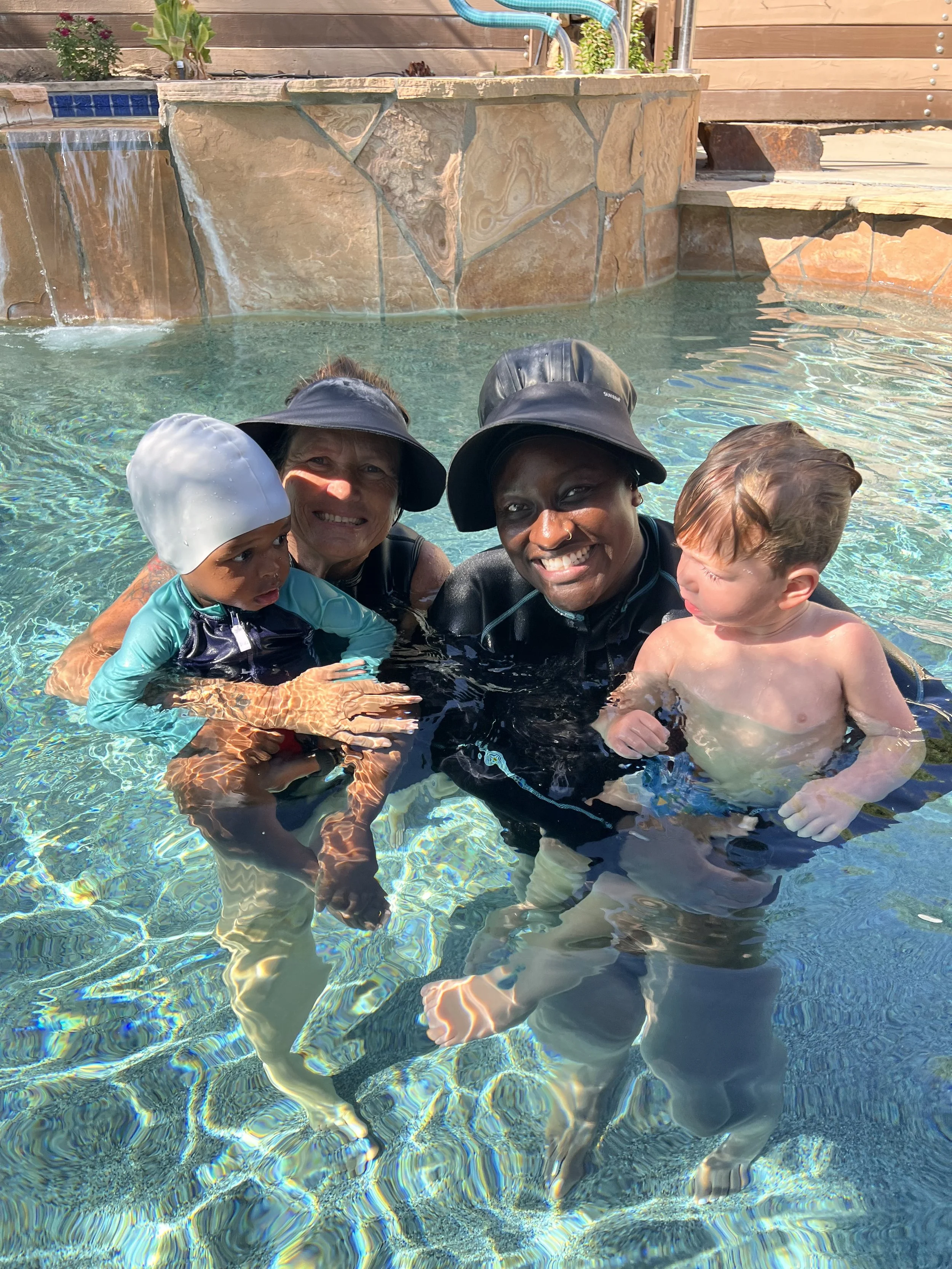Two adult women and two young children enjoying a swim in a backyard pool on a sunny day.