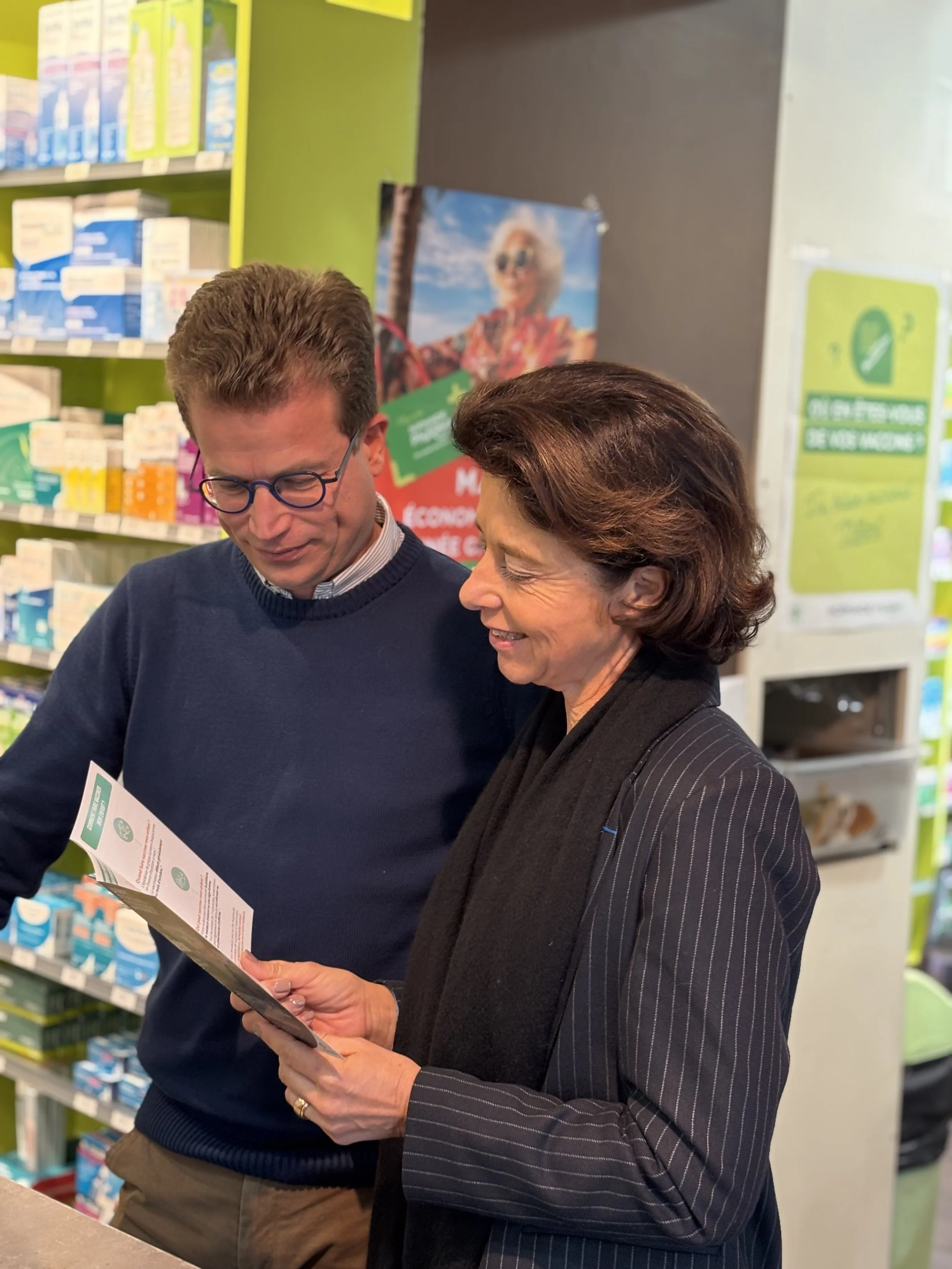 Deux personnes discutent dans une pharmacie ou un point de vente de médicaments, lisant un document ensemble.