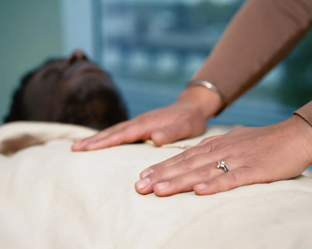 A person performing Reiki on a man lying on a bed, with a hand on his chest.