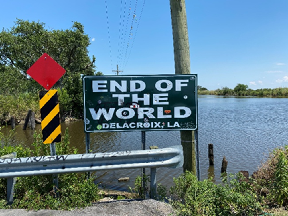 An image of Lake Borgne where there is a black and white sign that says "End of the World, Delacroix, Louisiana".