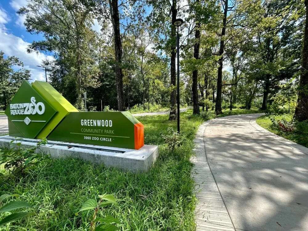 An image of a green sign on a concrete slab designating the location of BREC ZOO Greenwood Park Entrance
