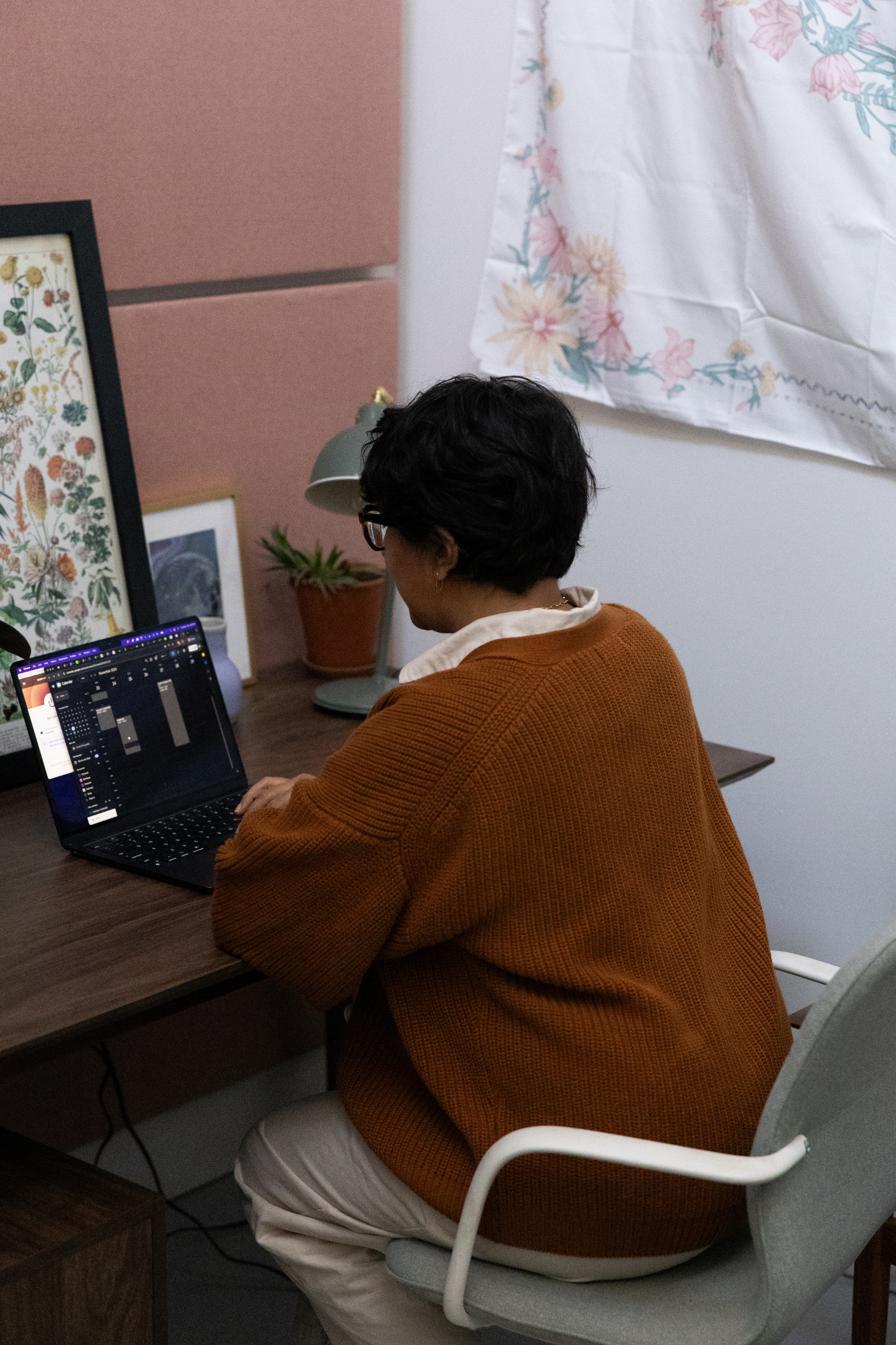 Person with short dark hair and glasses sitting at a desk working on a laptop