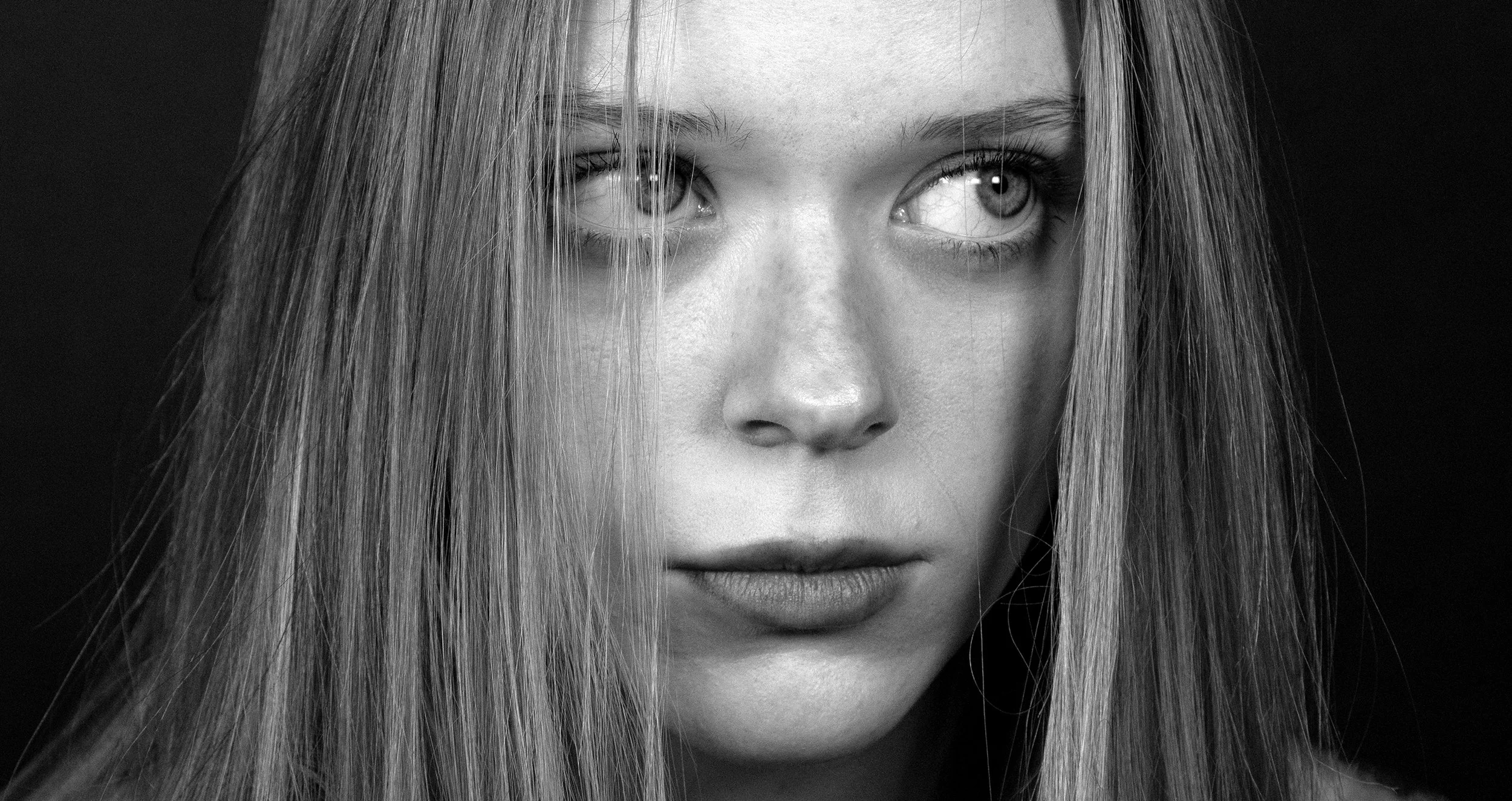 Close-up black and white photograph of a young woman's face with long hair, showing her eyes, nose, and lips.