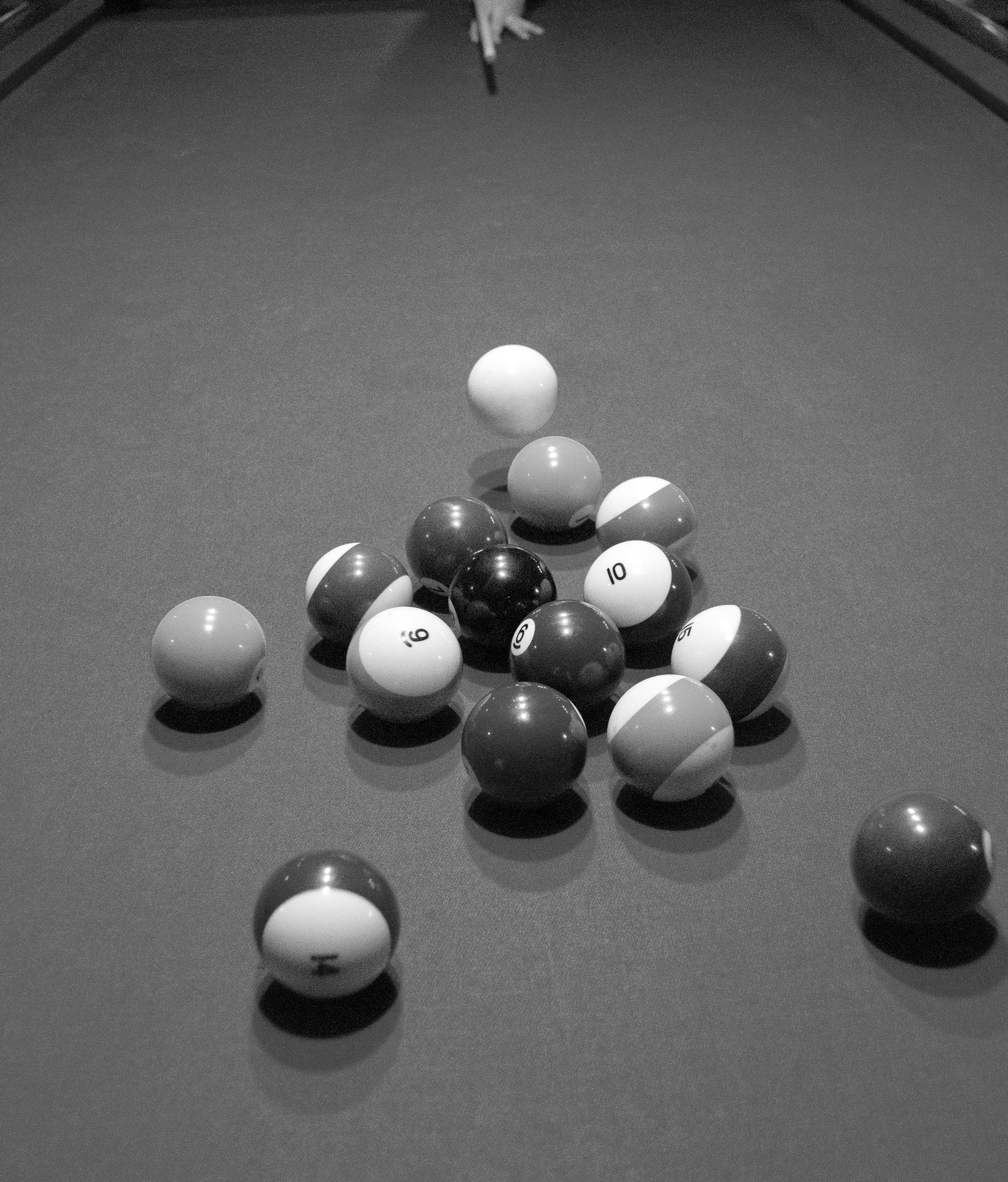 A black and white photo of a billiards table with pool balls scattered on the surface.