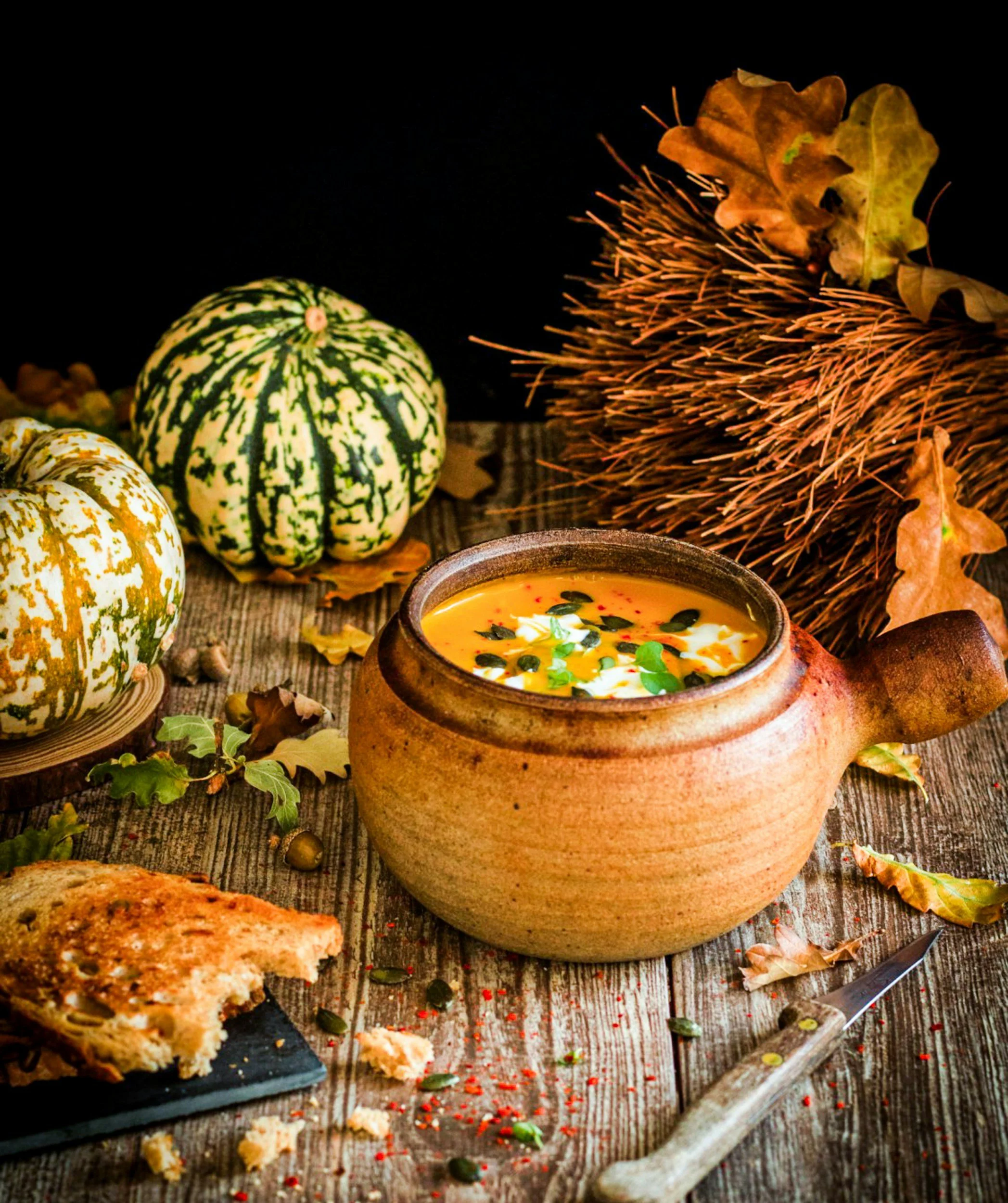 squash soup in clay serving bowl on a table with gourds and bread