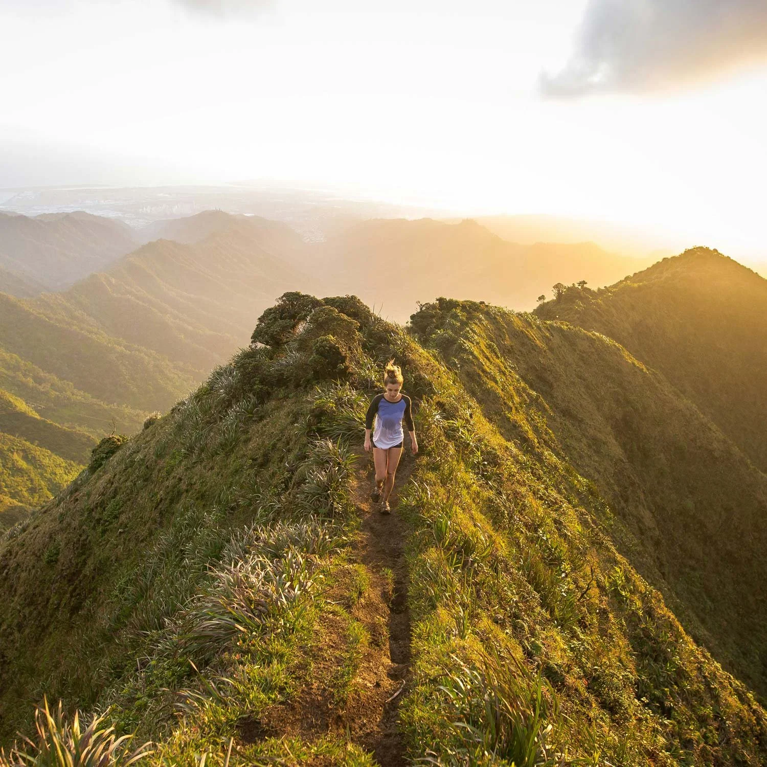 Woman walks on a skinny mountain trail wearing shorts and t-shirt.