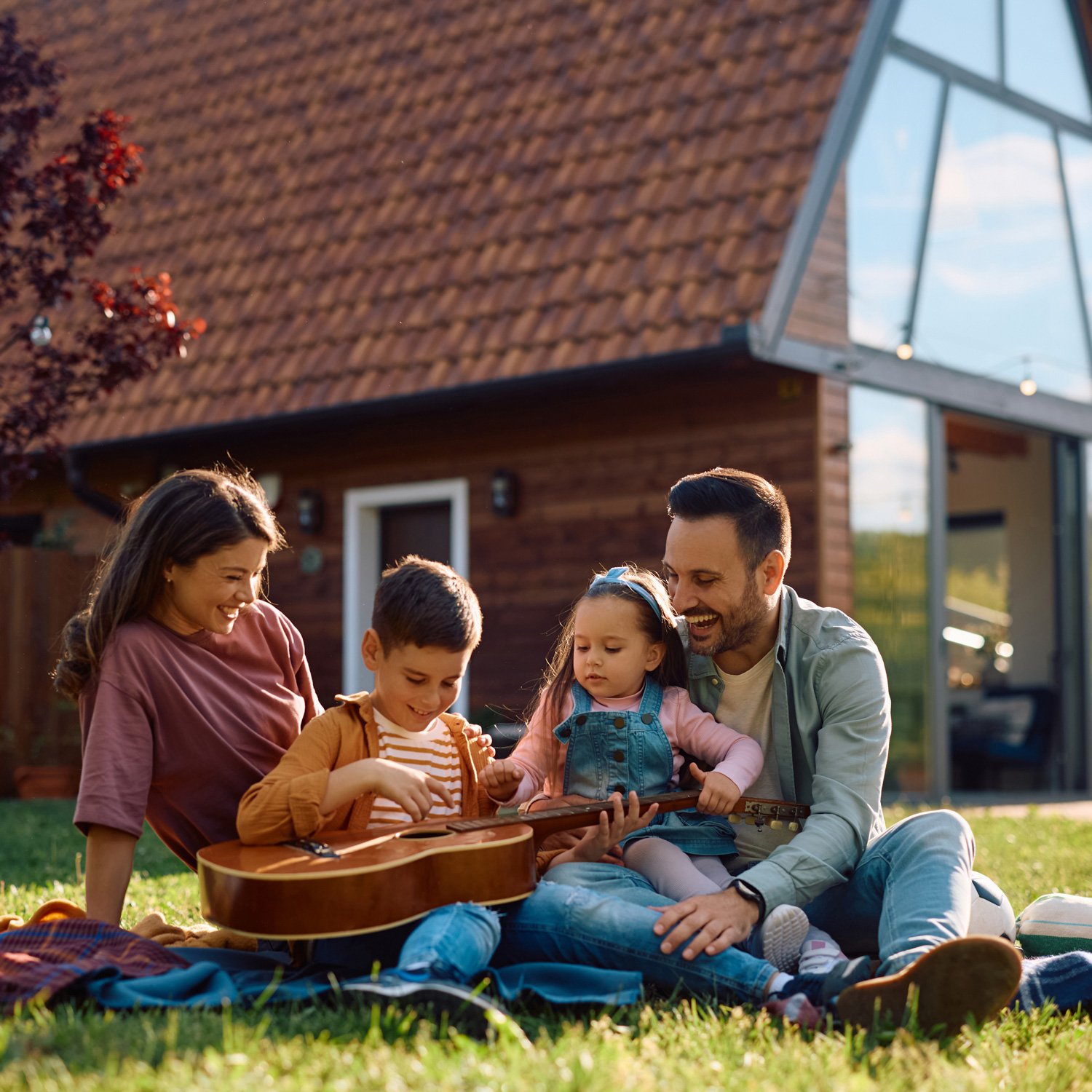Dad and mom play guitar with kids outside on a blanket.