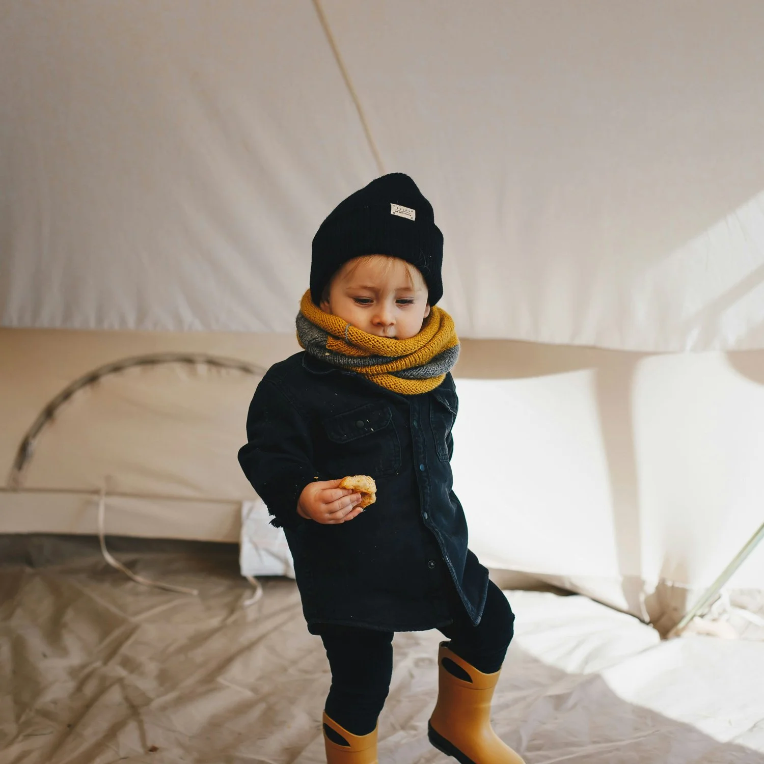 Small boy eats a snack in the tent.