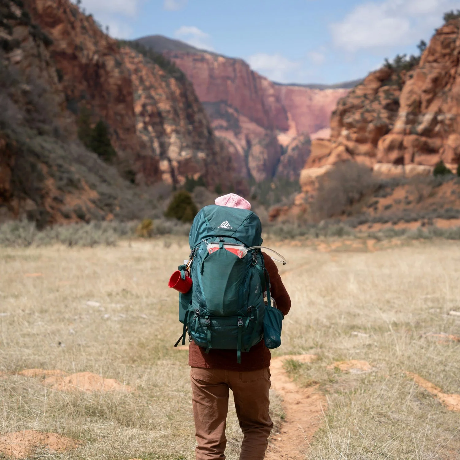 Backpacker with a turquoise backpack walks a canyon trail.