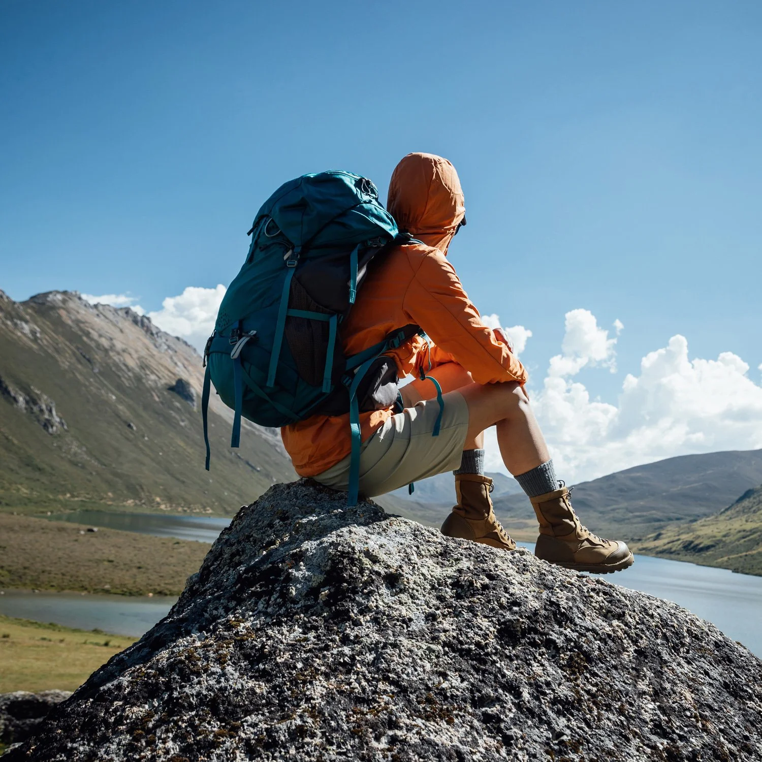 Backpacker rests on a rock near a mountain lake.