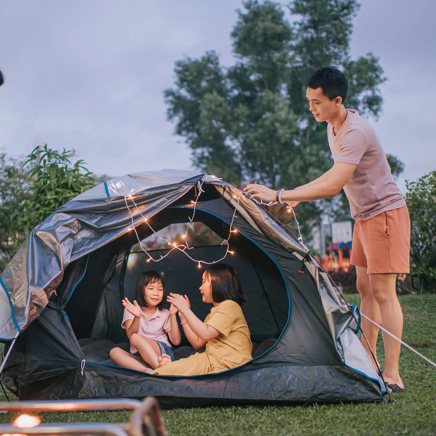 Dad strings lights on a tent while his girls play inside the tent.