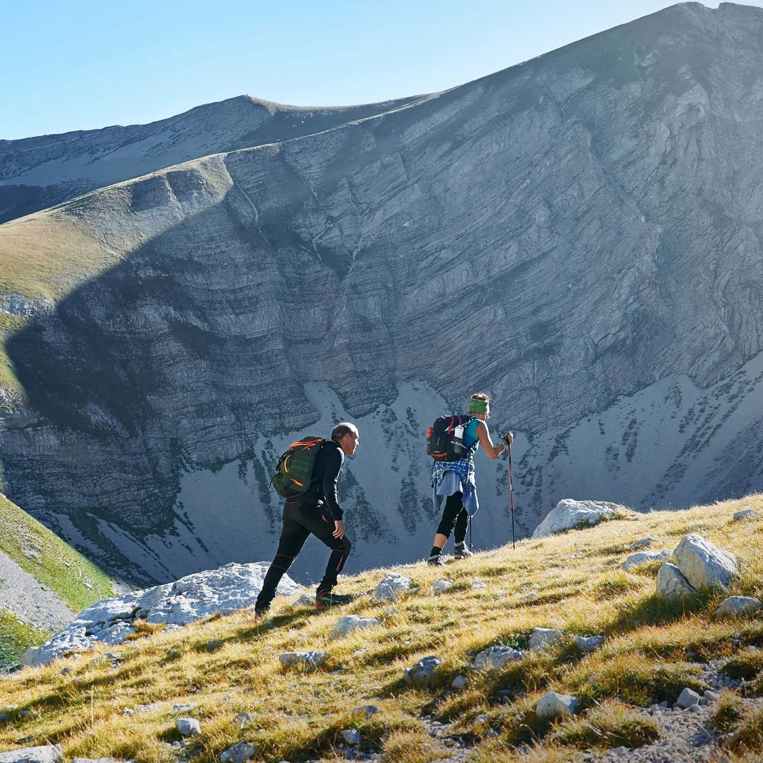 Two hikers wear several layers of clothing while hiking up a mountain.