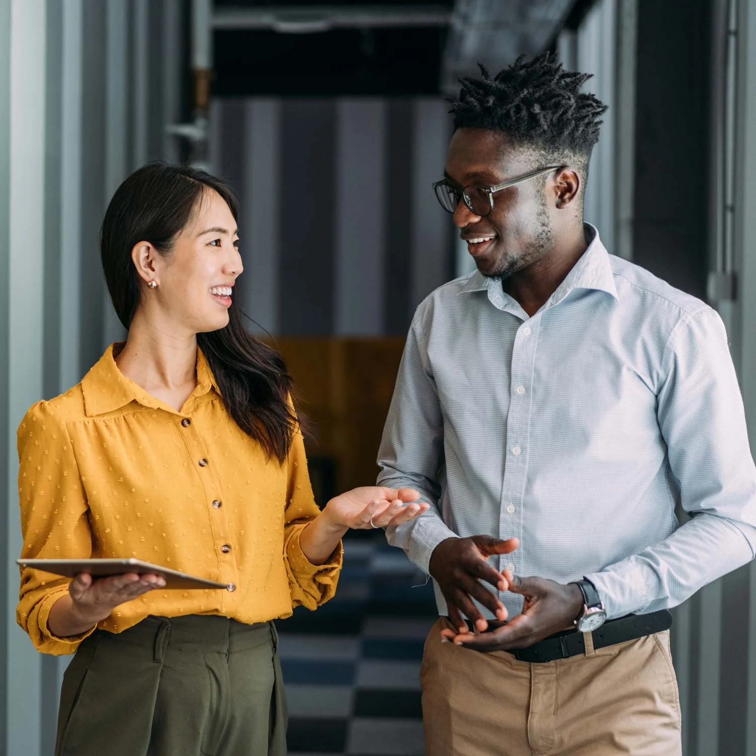 Two employees walk down the hallway and discuss a project.