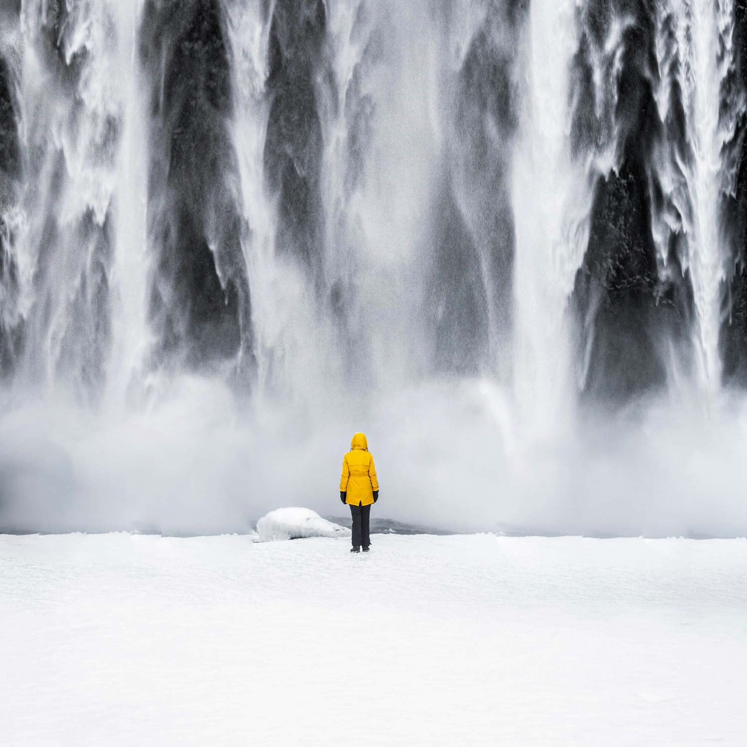Person stands in front of a water fall wearing a raincoat.