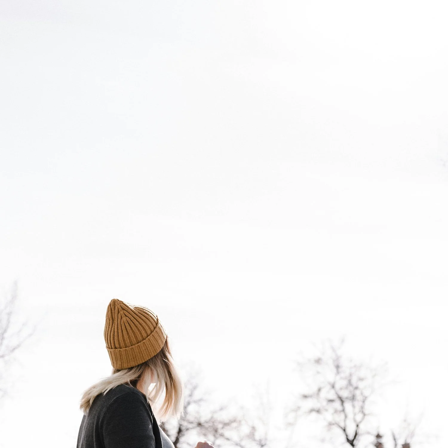 A woman in a gold winter hat walk through the trees.