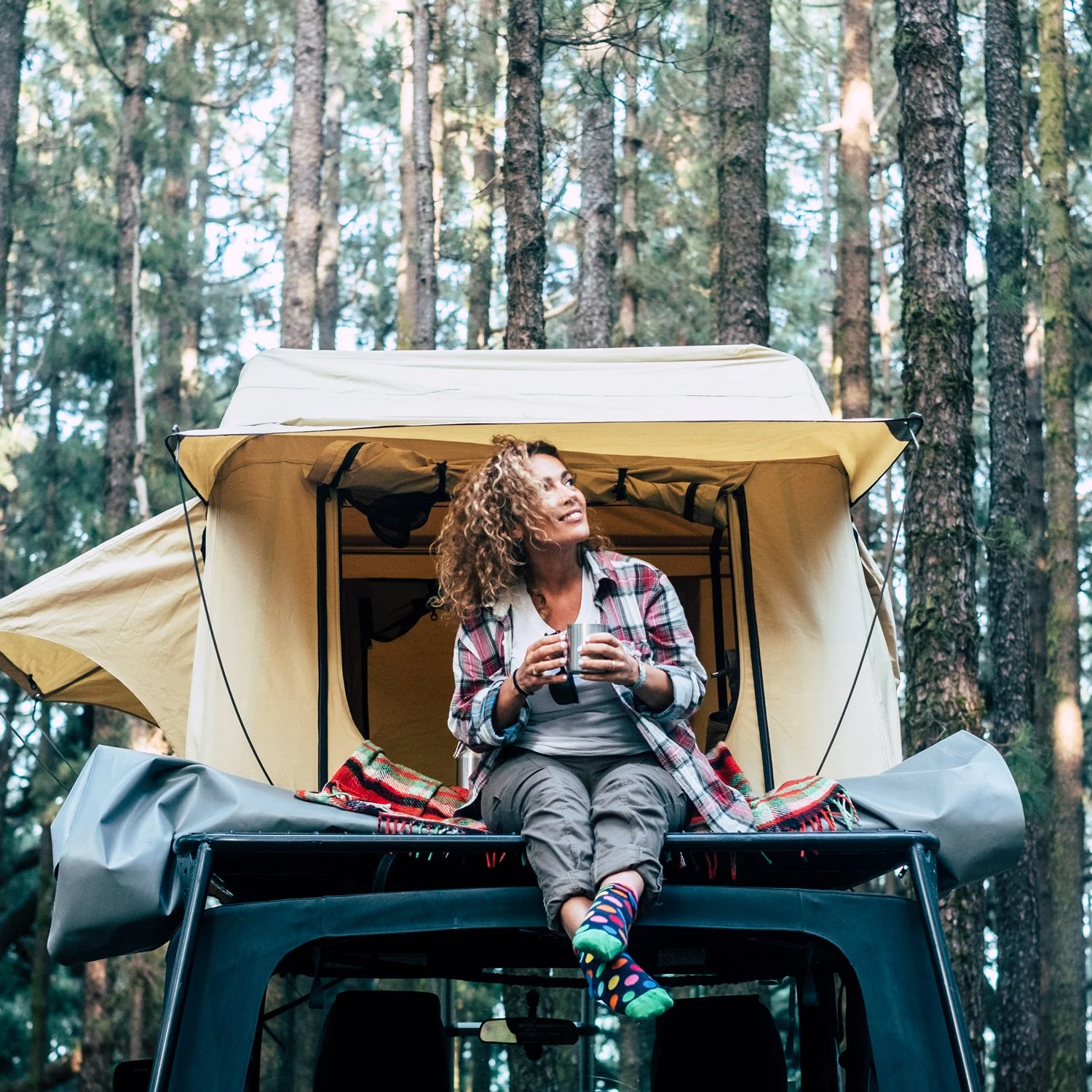 Woman sits outside of rooftop tent.