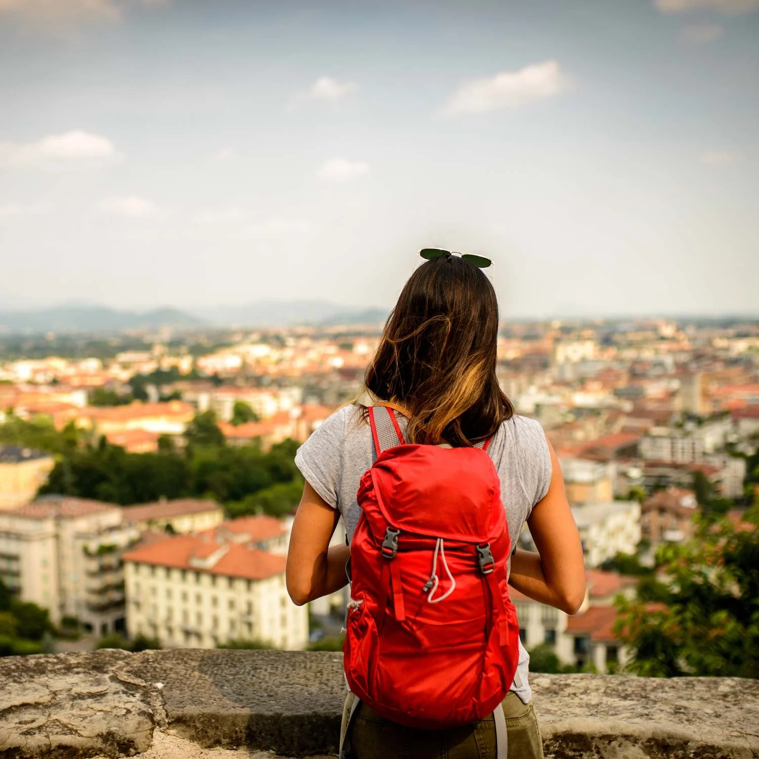 Female hiker stands by wall and looks down at city.
