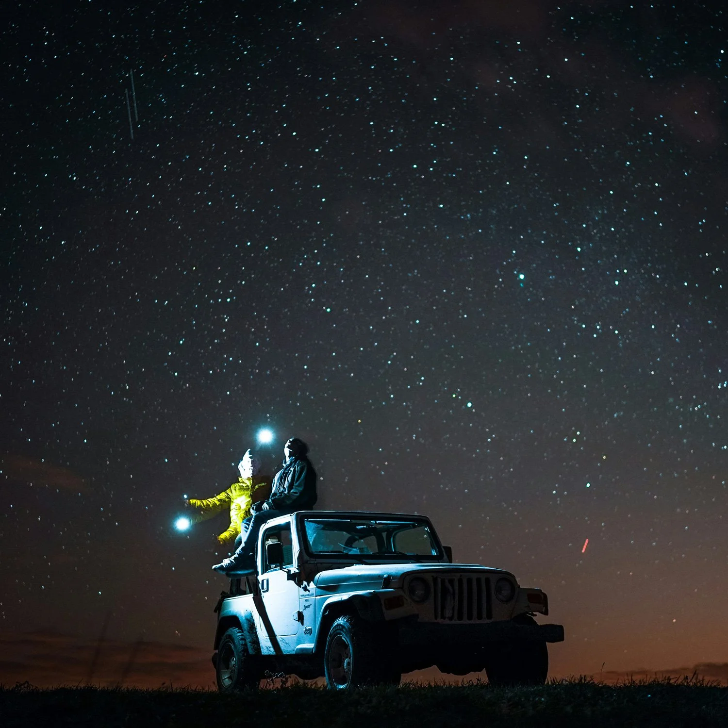 Two people sit on a jeep at night with the stars shining above.