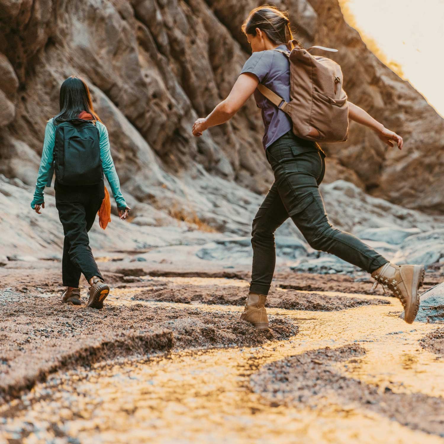 Two female hikers walk through a small stream.