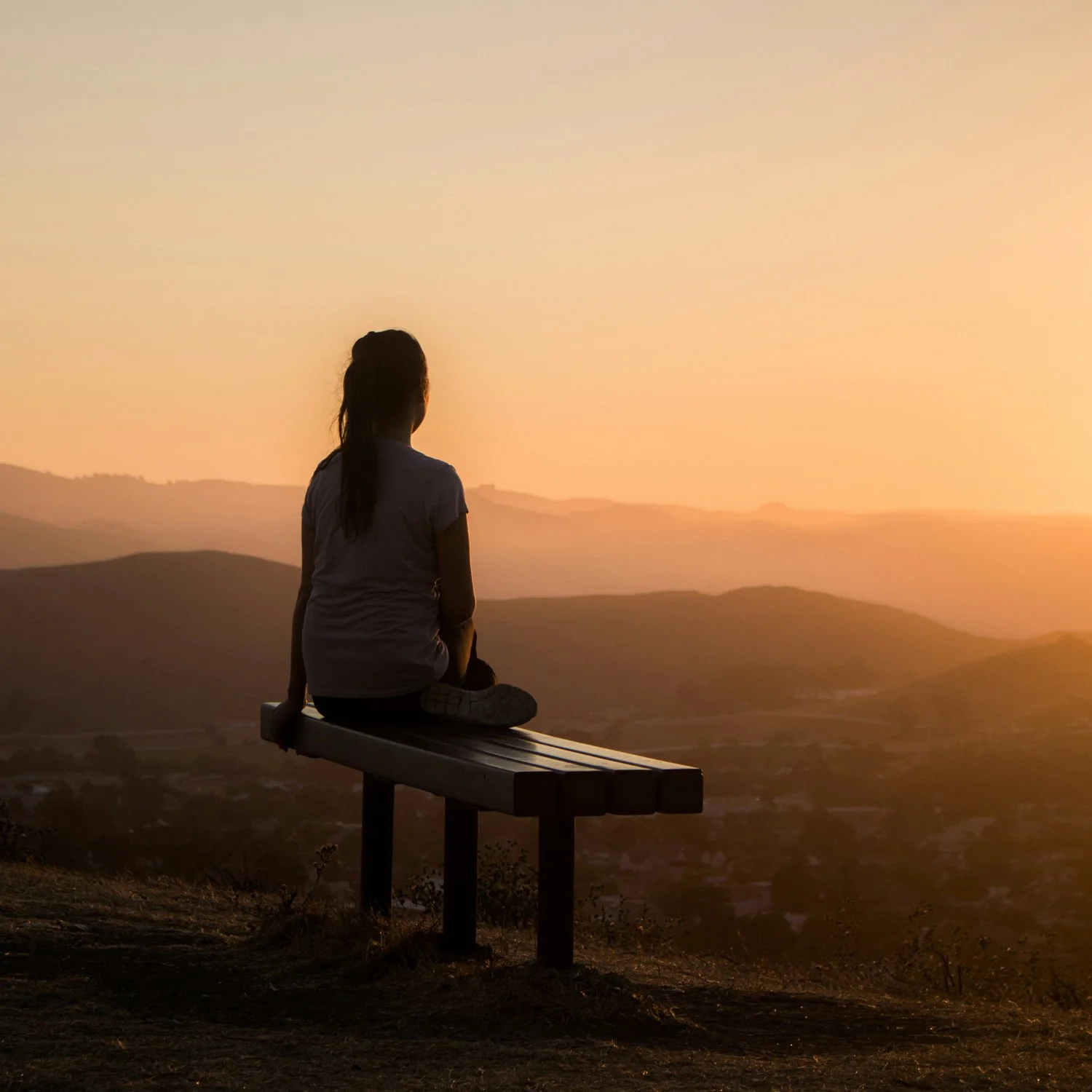 Woman sits on a bench taking in the sunset on her day off.
