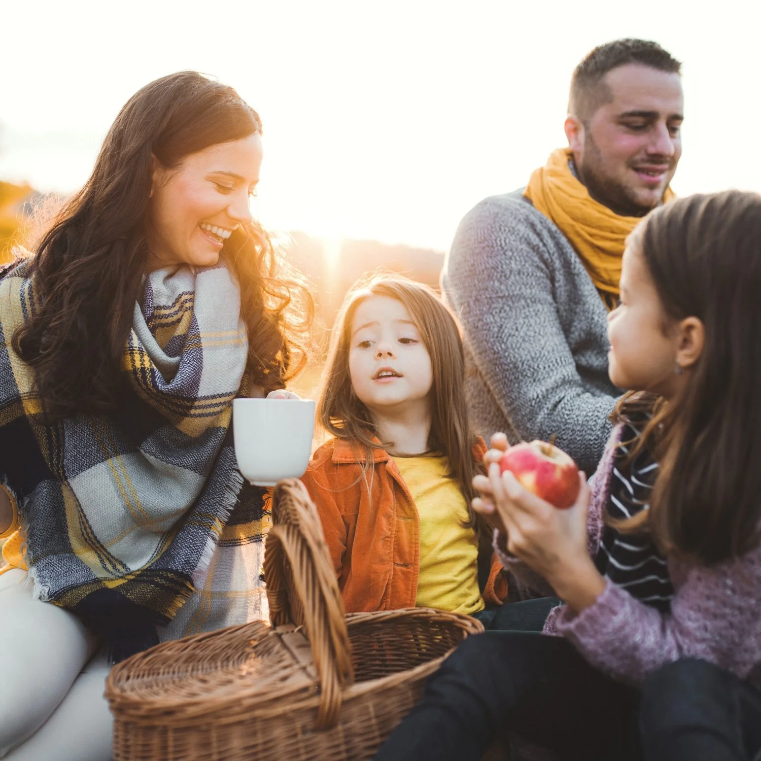 Family drink hot drinks and eats apples at a picnic.