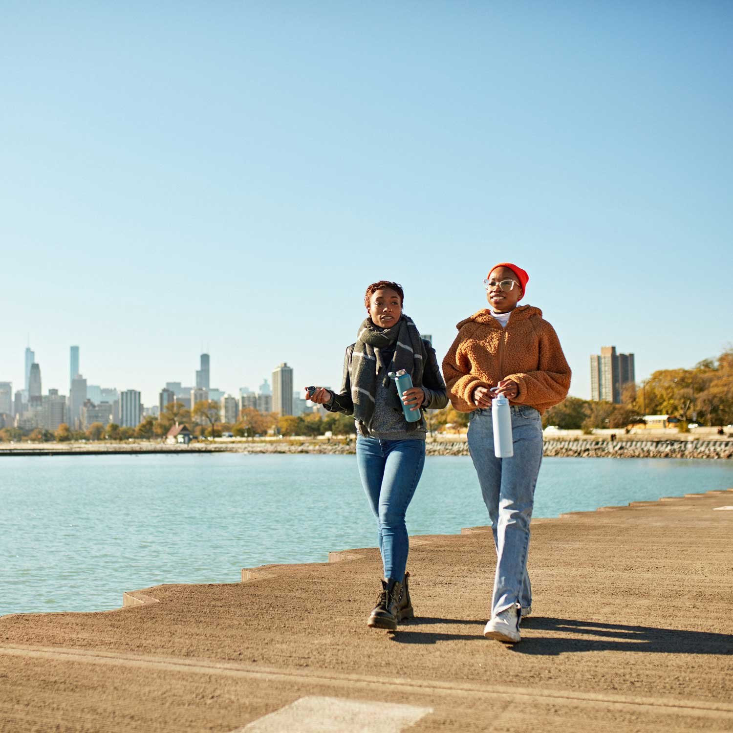 Two people stay active outdoors and walk along the waters edge.