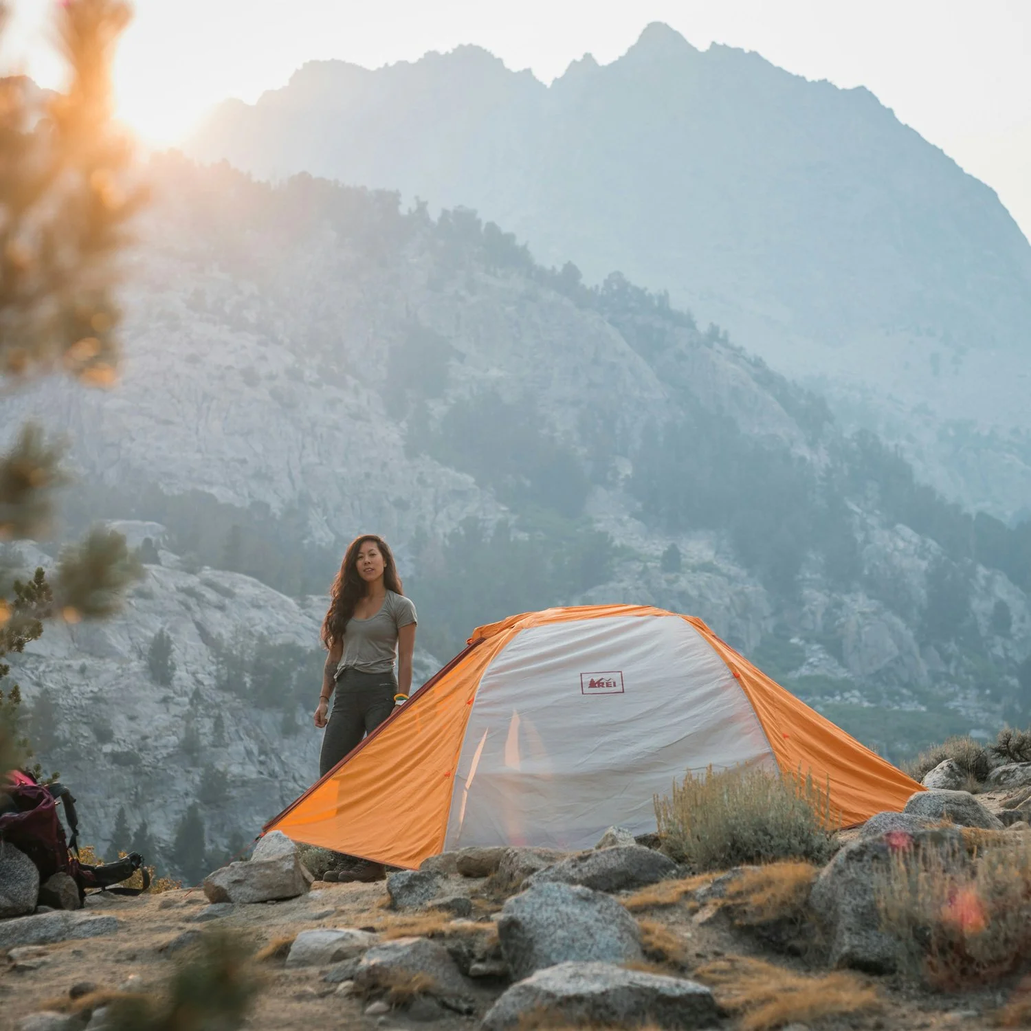 Woman stands by orange and gray backpacking tent.