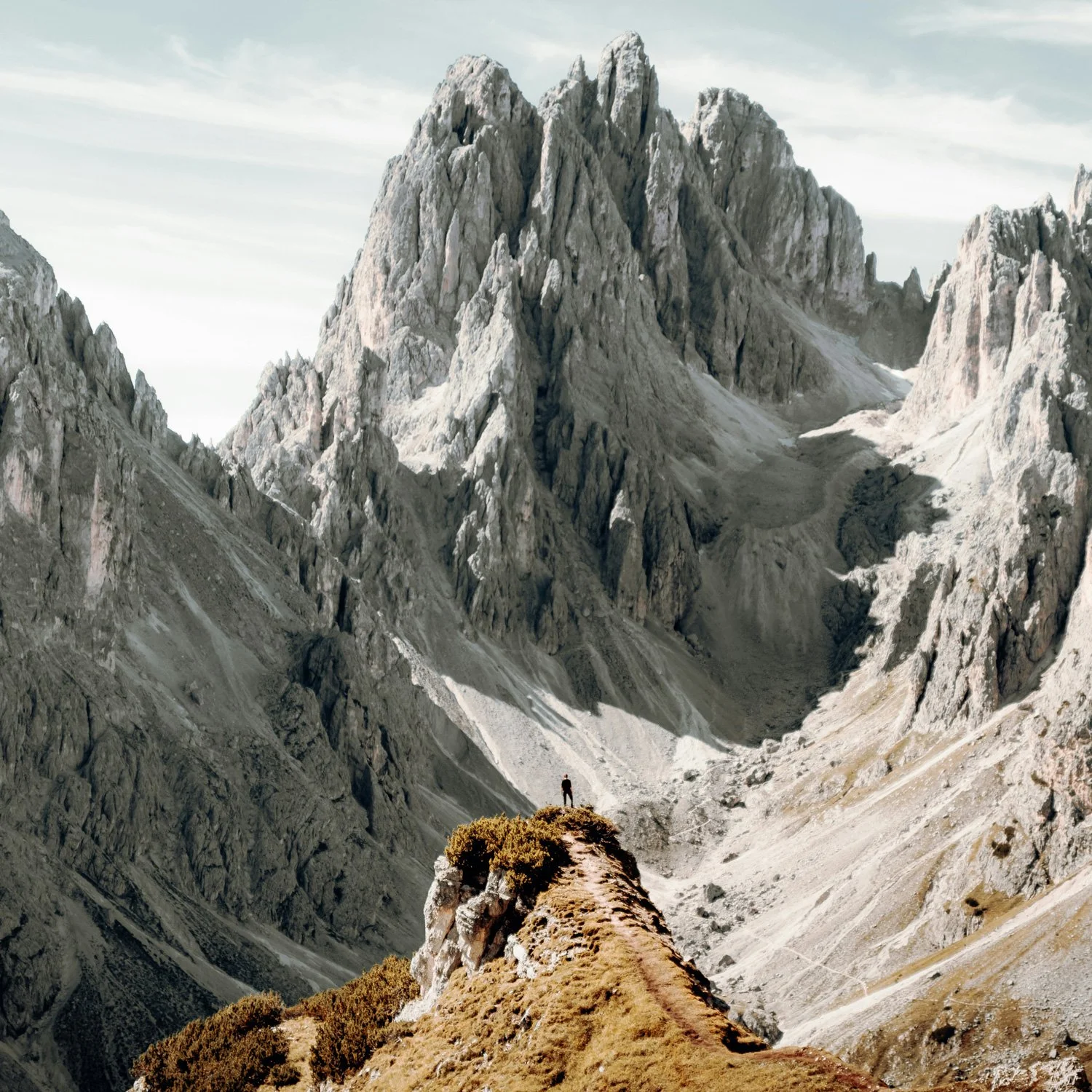 Massive cliffs overshadow a small hiker standing at their base.