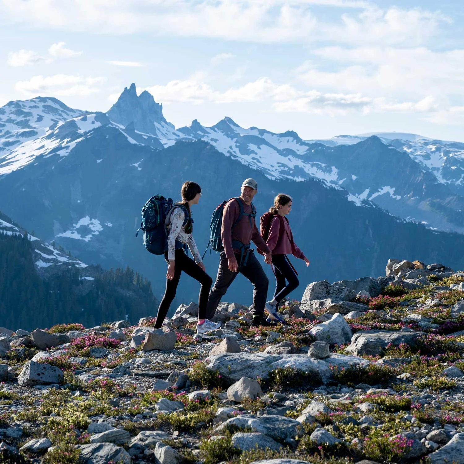 A dad and two daughters hike along a mountain trail.