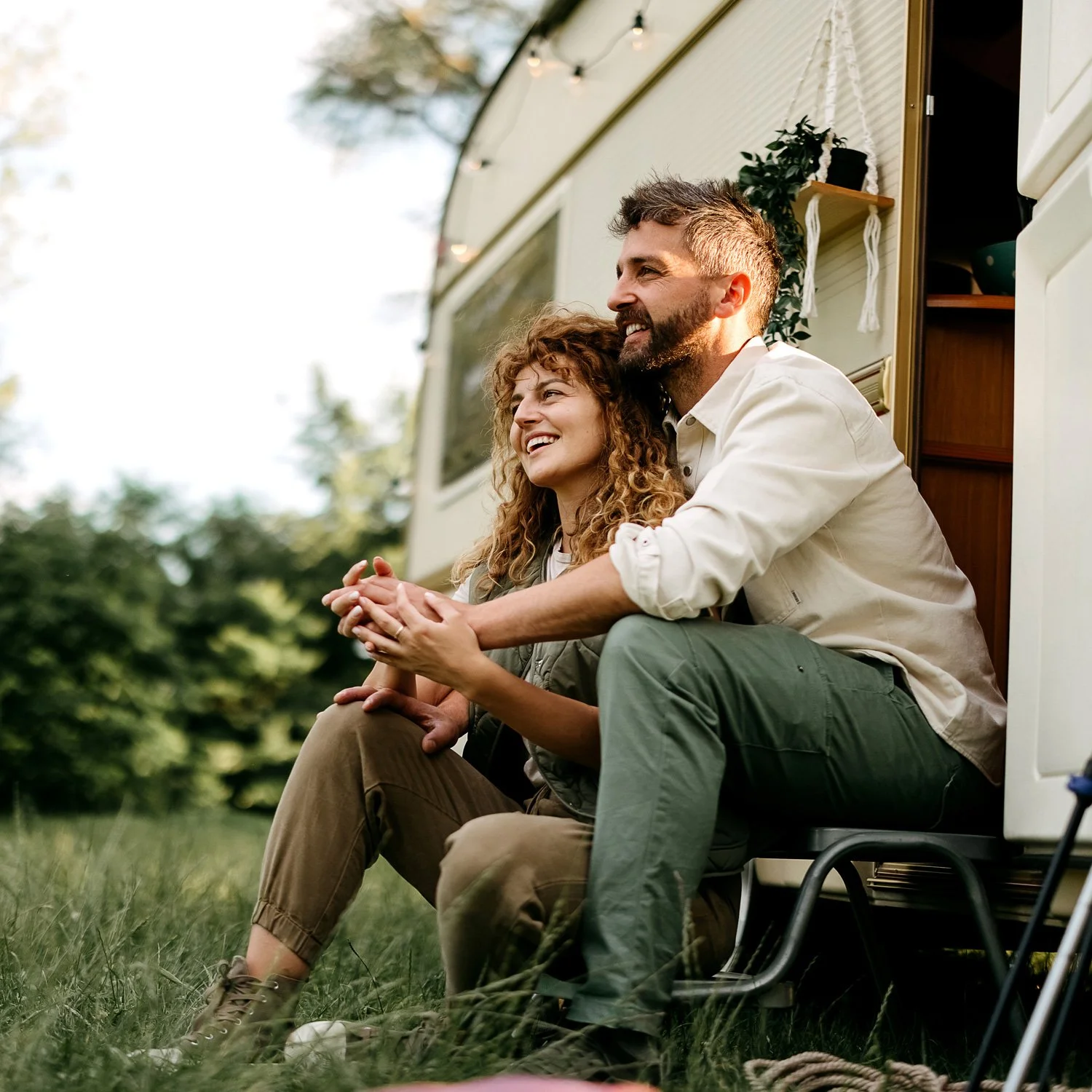 A couple sits outside their RV on a camping trip.