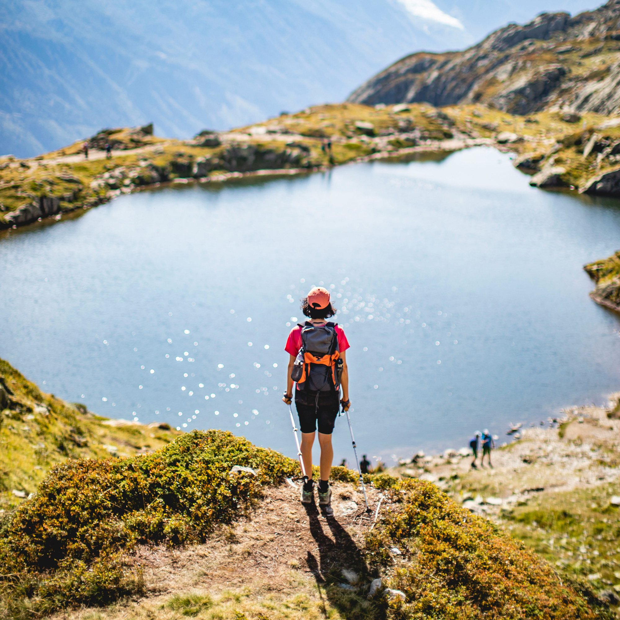Female hiker stand above a mountain lake and looks out on the scenery.