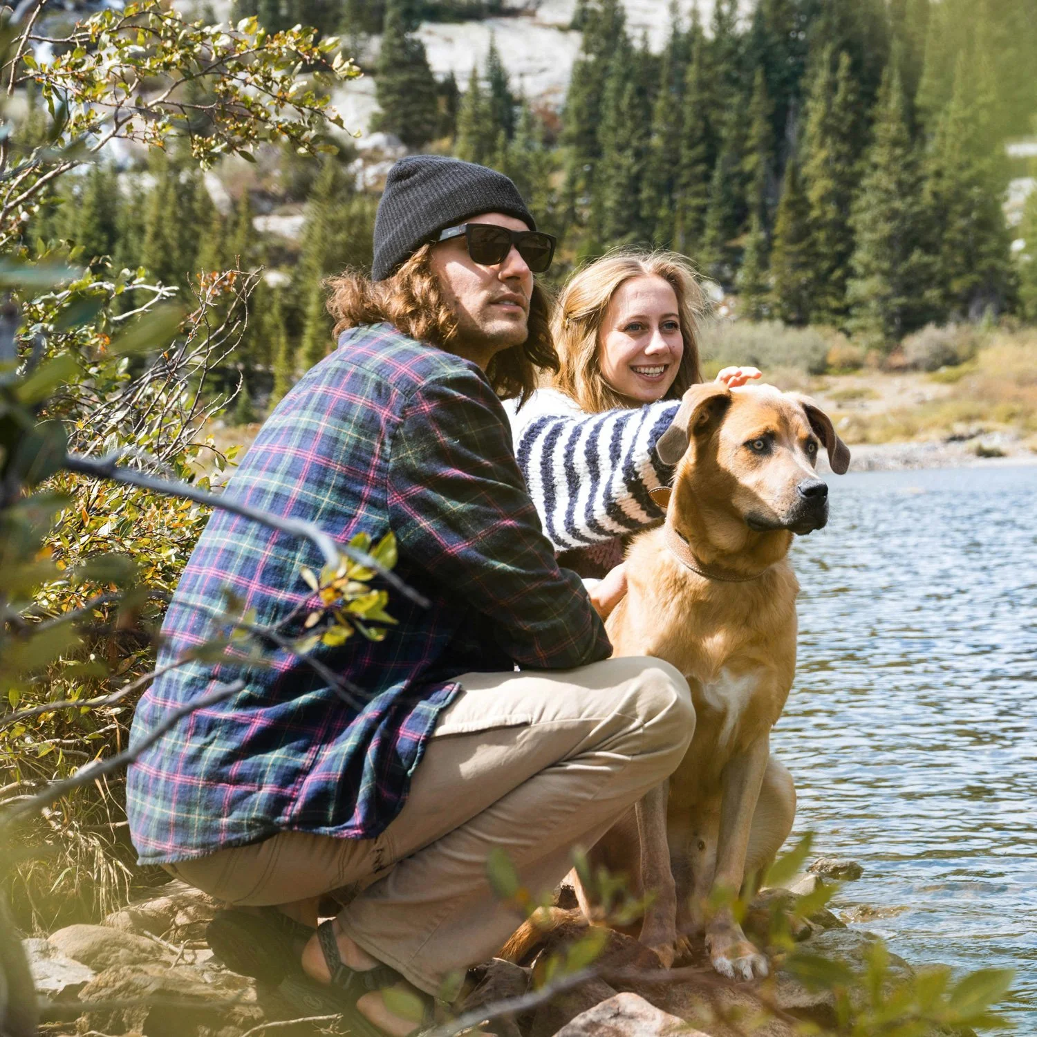 A man, woman, and dog sit by a mountain lake.