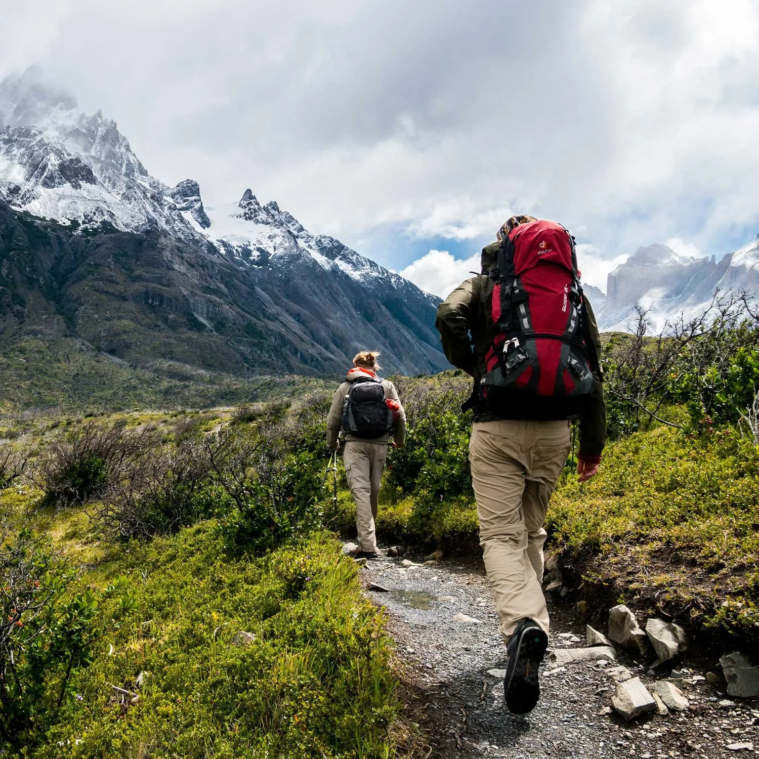 Two beginner backpackers hike at the base of a mountain.