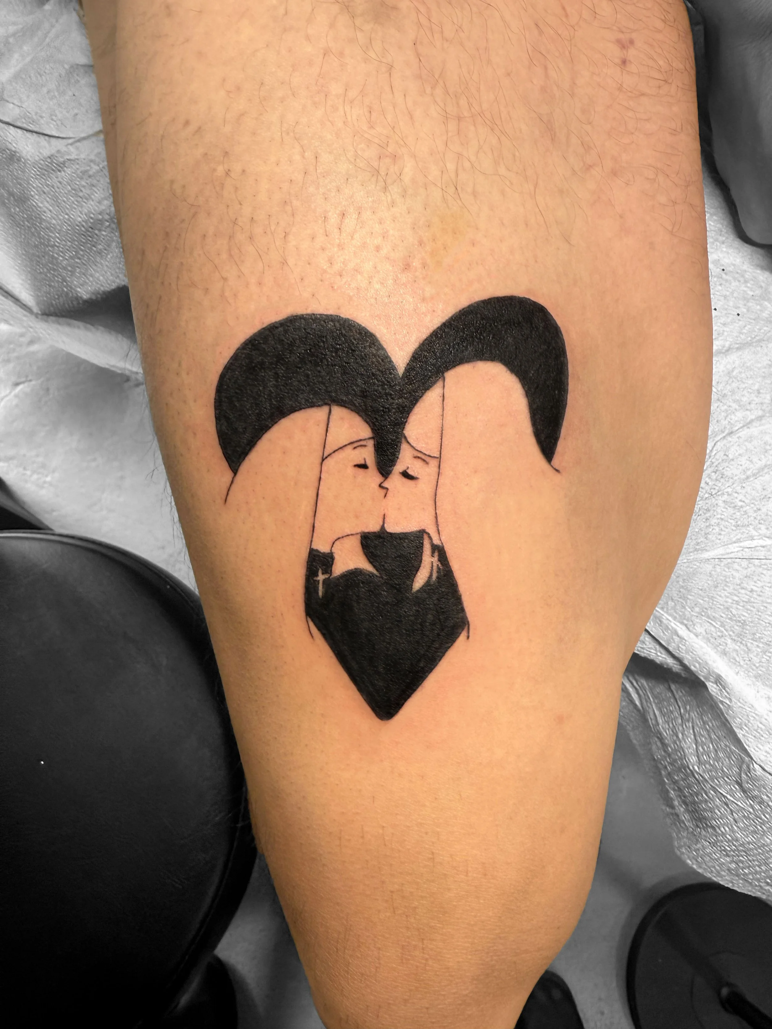 Tattoo of a couple kissing, forming the shape of a heart with their faces and hair, on a person's thigh.